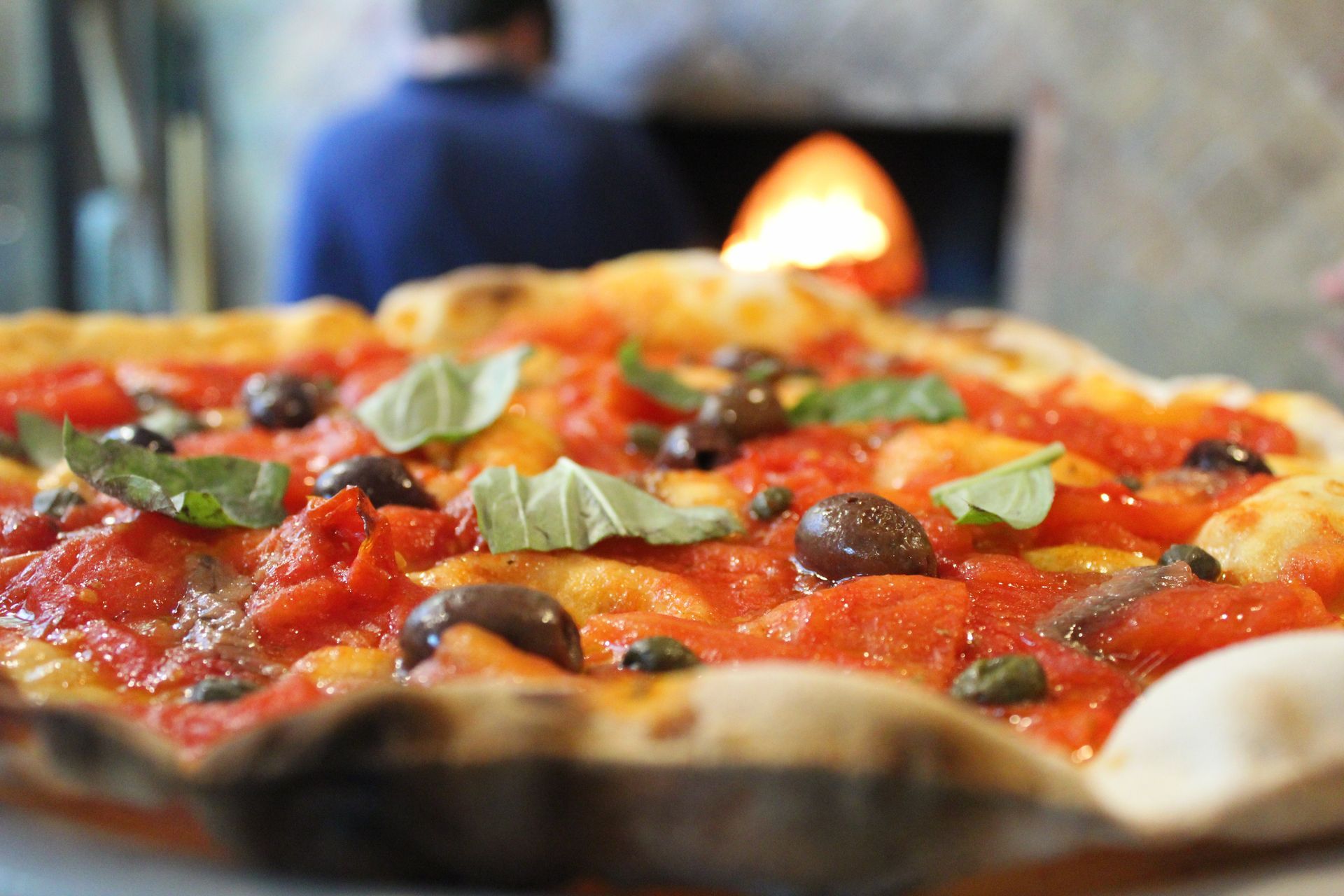 Tre pizze su supporti di metallo con un forno sullo sfondo. Una con fragole e spinaci.