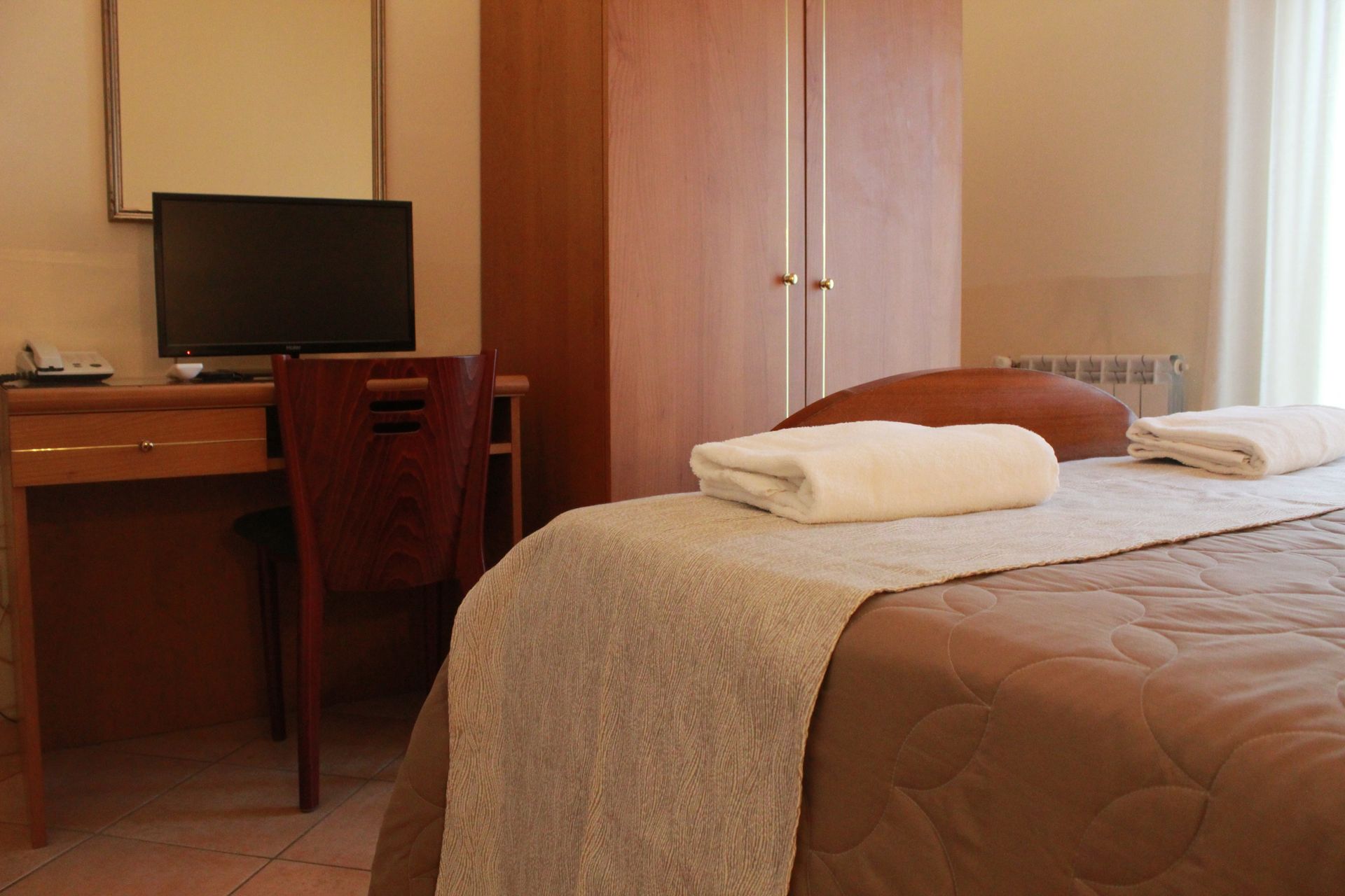 Camera d'albergo con letto, scrivania, armadio e TV.