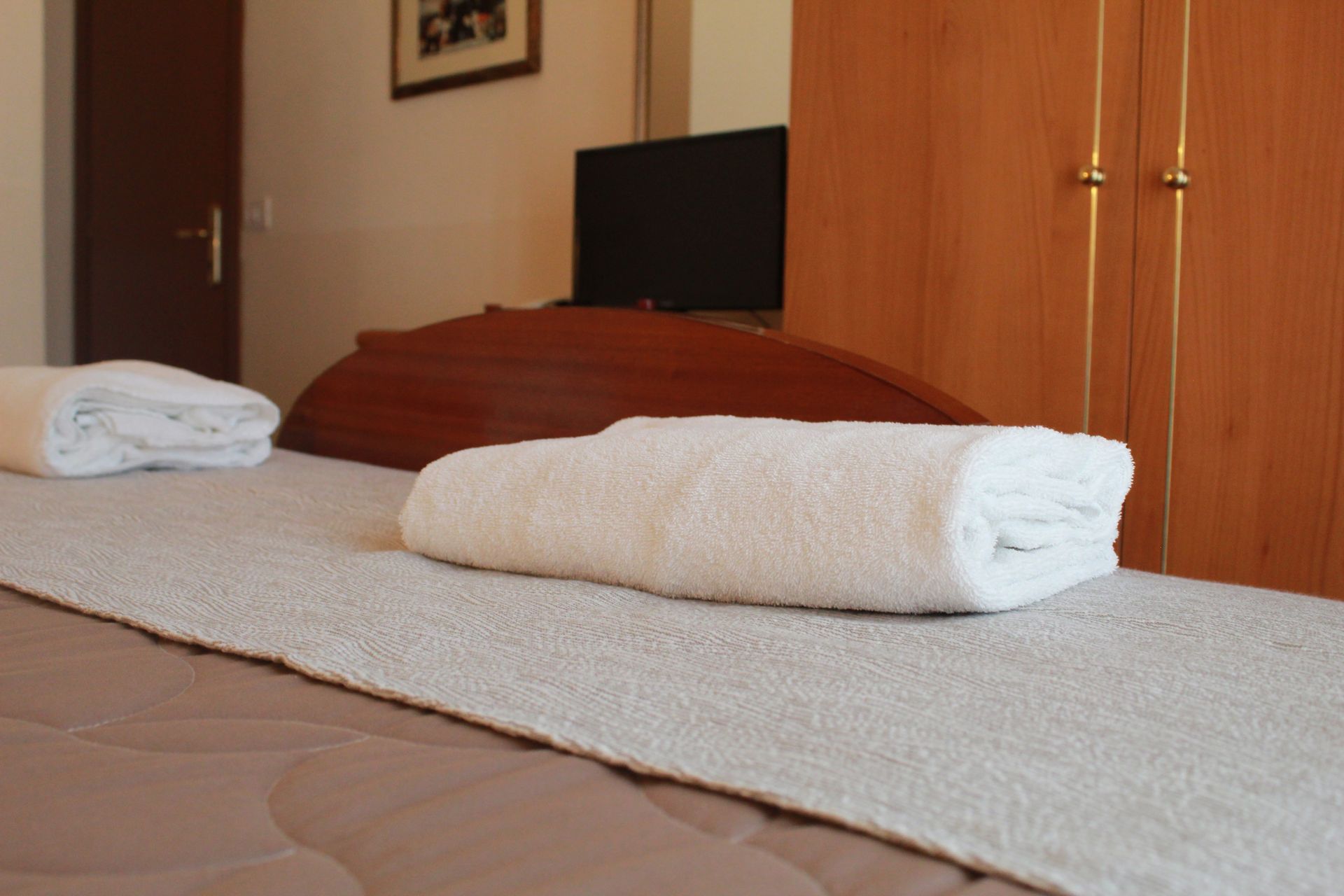 Letto in una stanza con asciugamani bianchi piegati, testiera marrone e televisione.