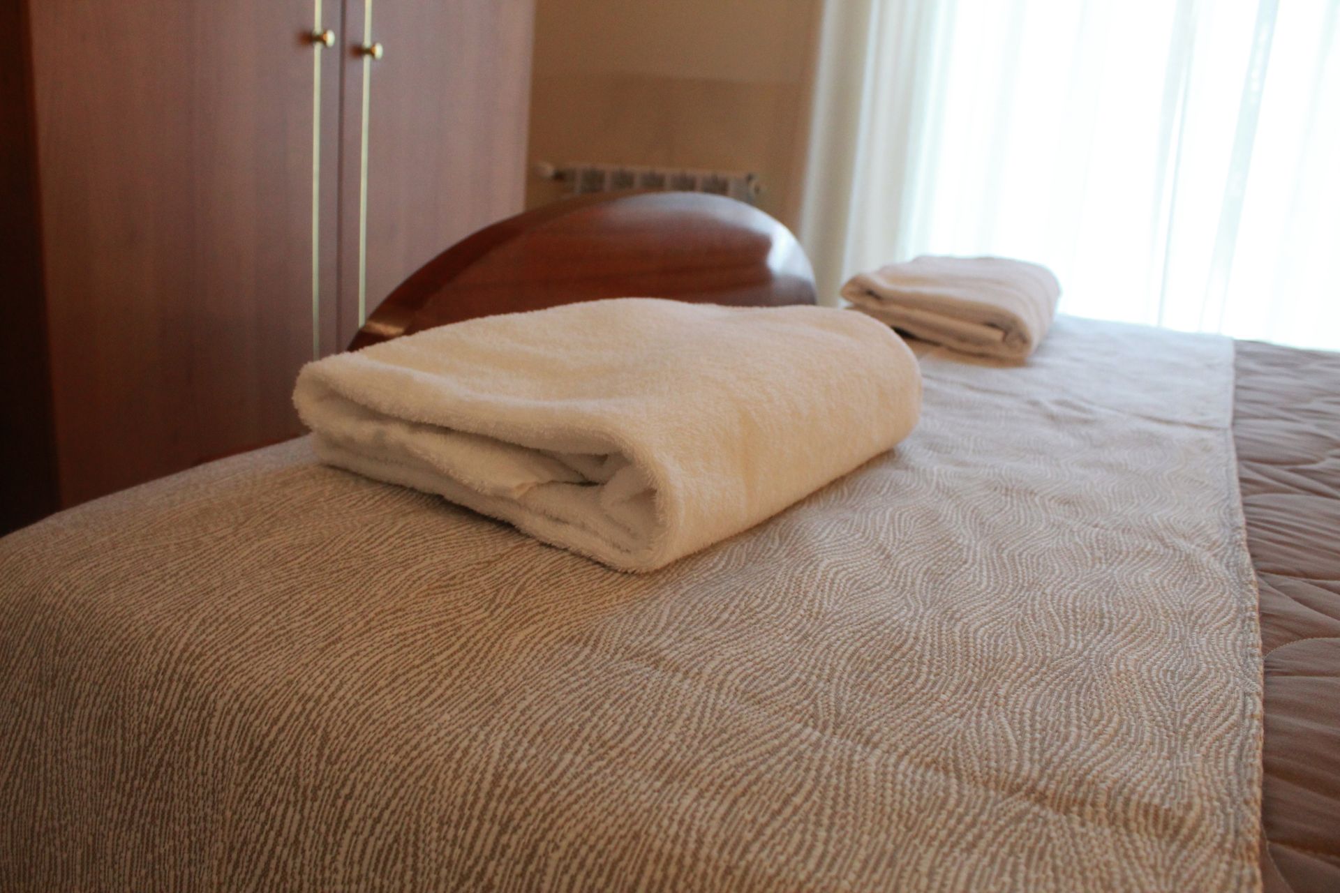 Lettino da massaggio con asciugamani piegati, vicino a una finestra e un mobiletto in legno.