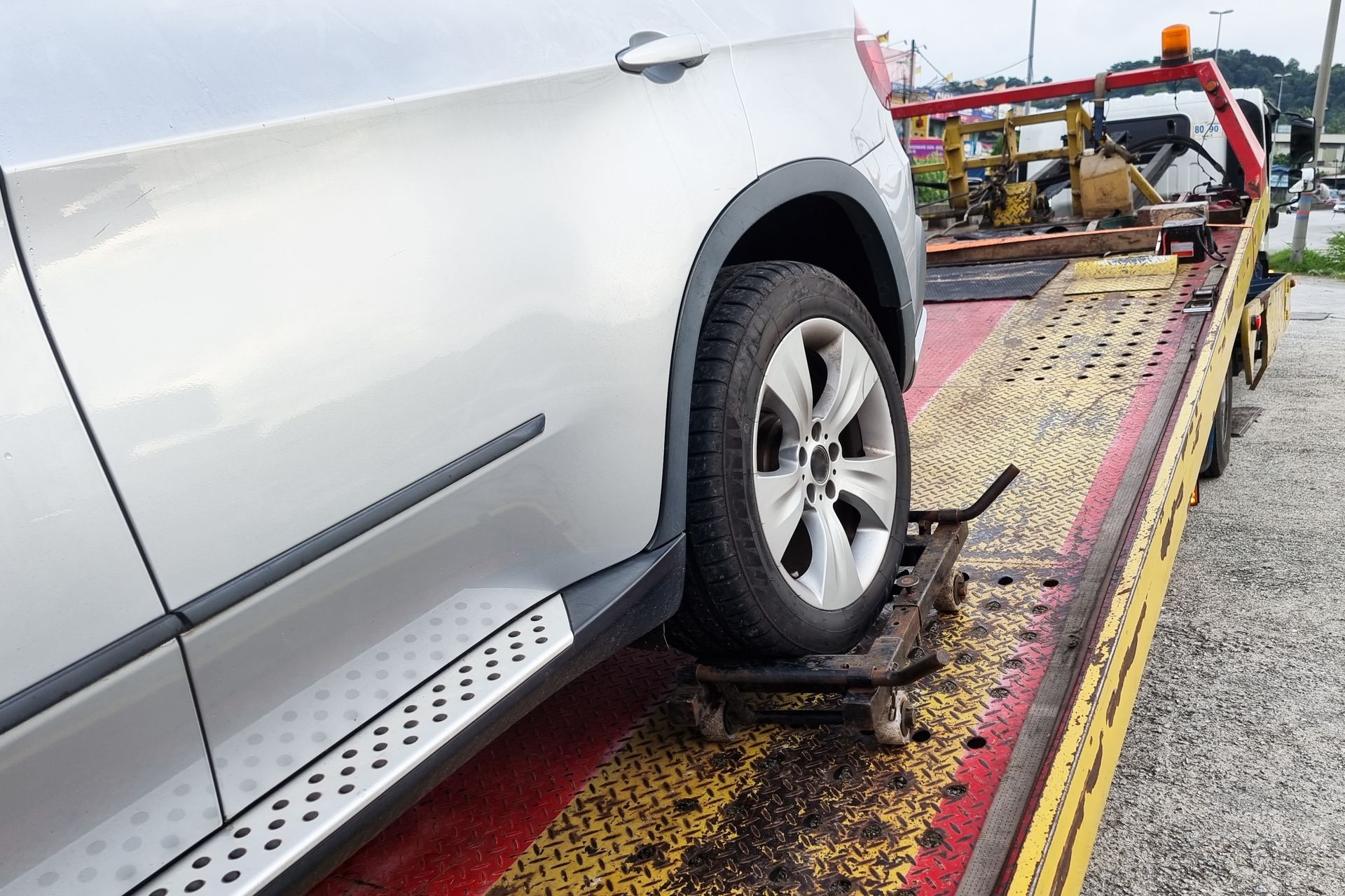 Silver SUV being towed by a yellow and red flatbed tow truck on a paved road.