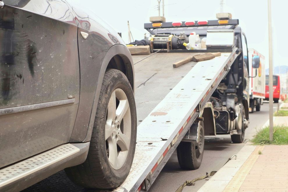 Black SUV being towed onto a flatbed tow truck on a city street.