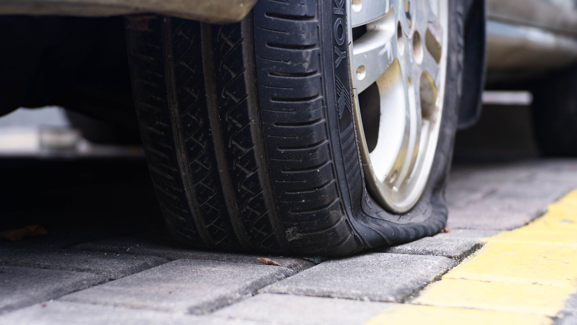 Flat tire on a car parked on brick pavement next to a yellow line.