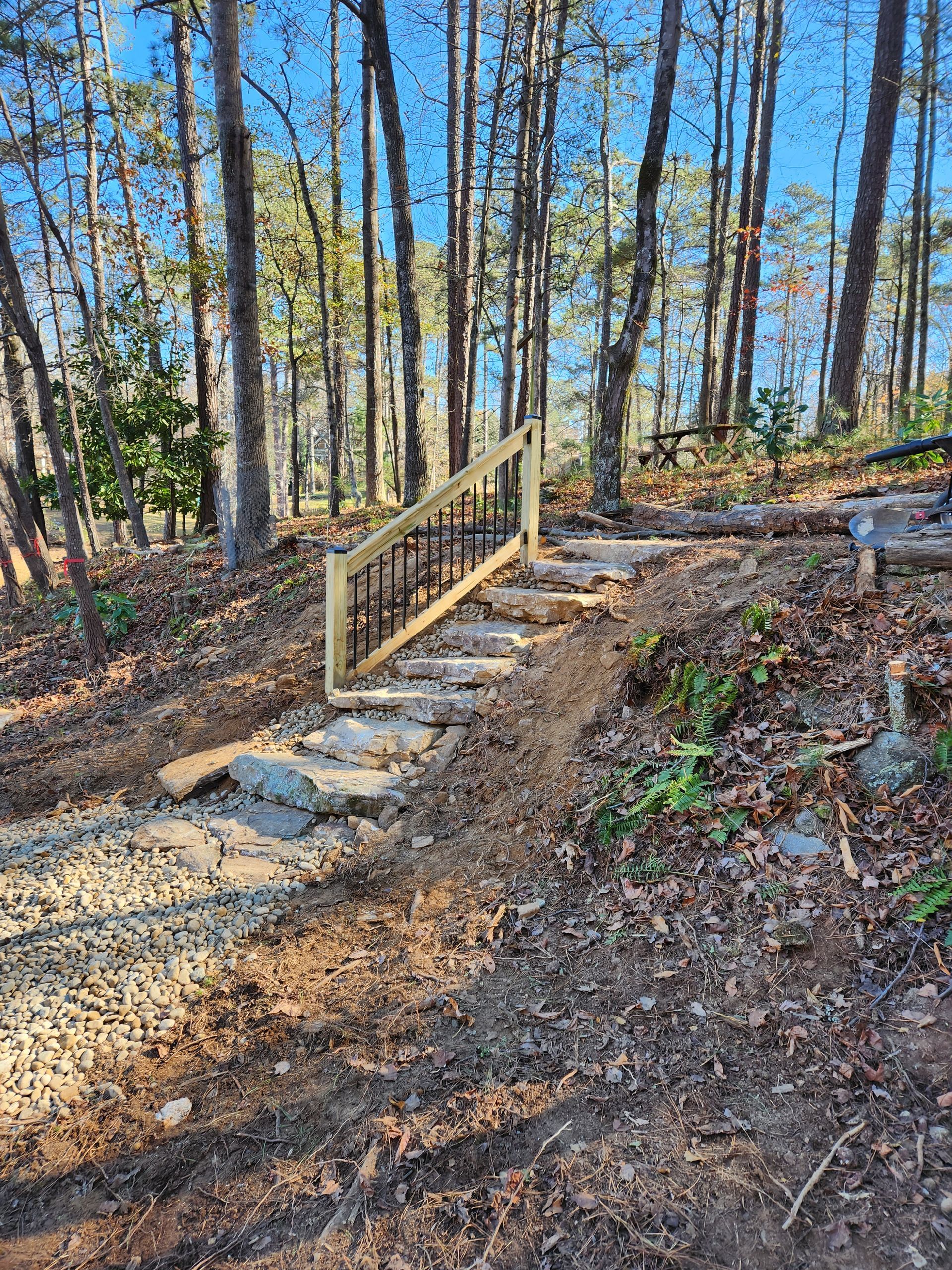 Stone steps with a wooden railing leading up a hillside in a forest.