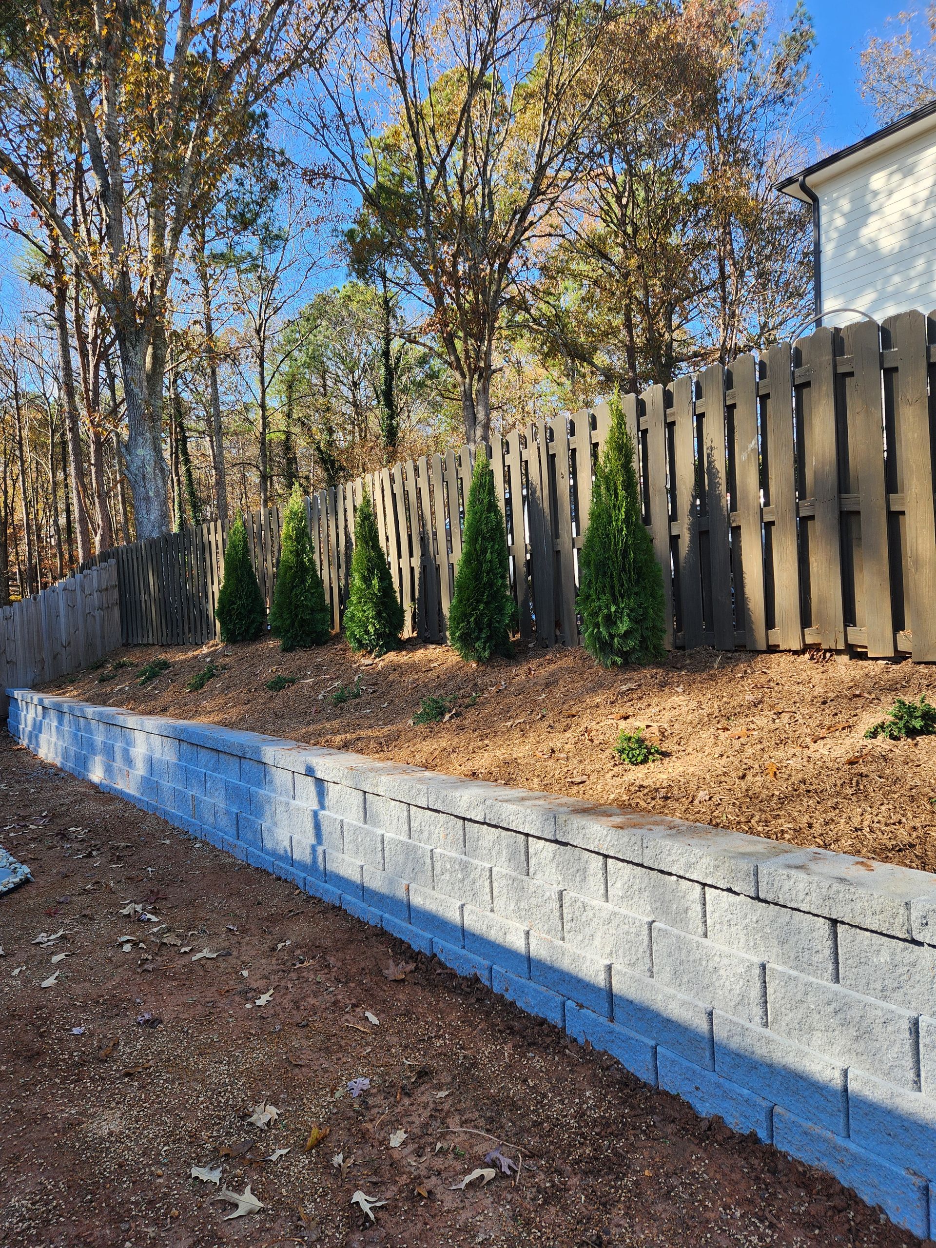 A retaining wall with a wooden fence and trees in the background.