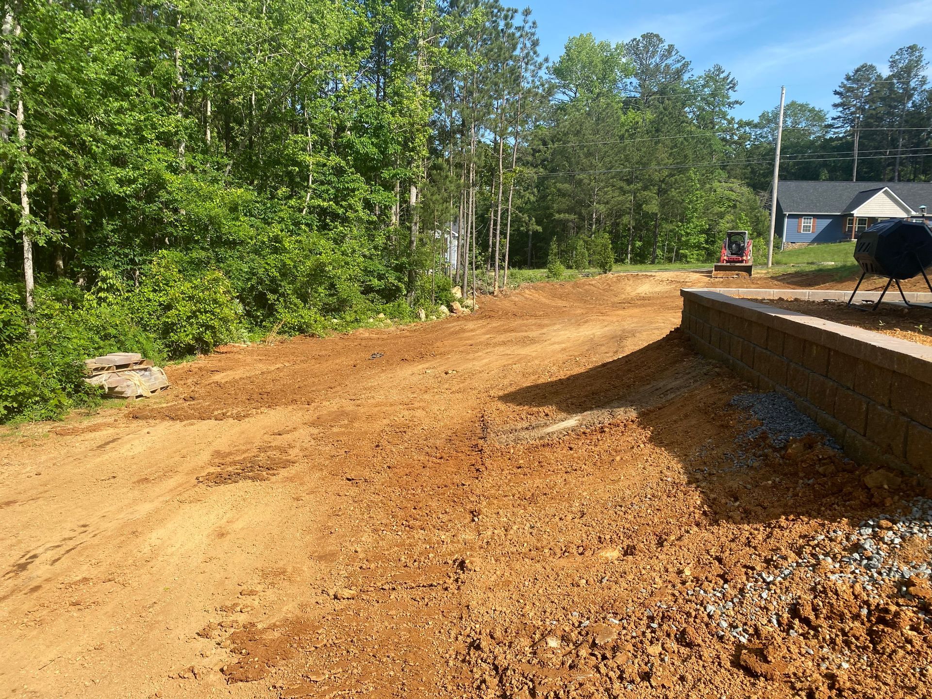 Dirt driveway under construction with trees in the background, a small red tractor.