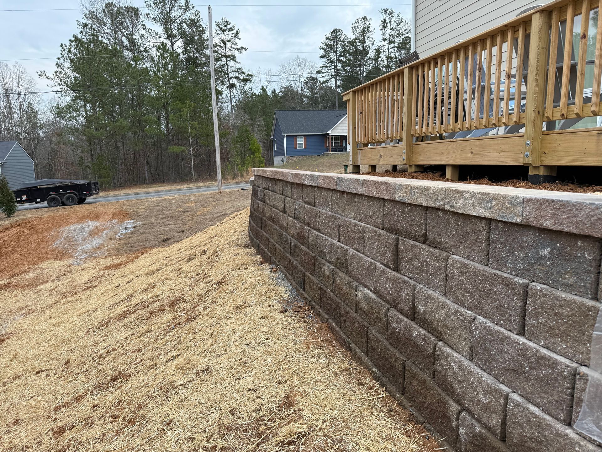 Retaining wall with a wooden deck on top, built on a sloped area with gravel and dirt.