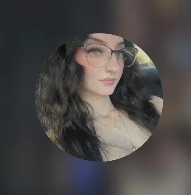 Woman with dark hair and glasses looking towards the left, wearing a necklace.