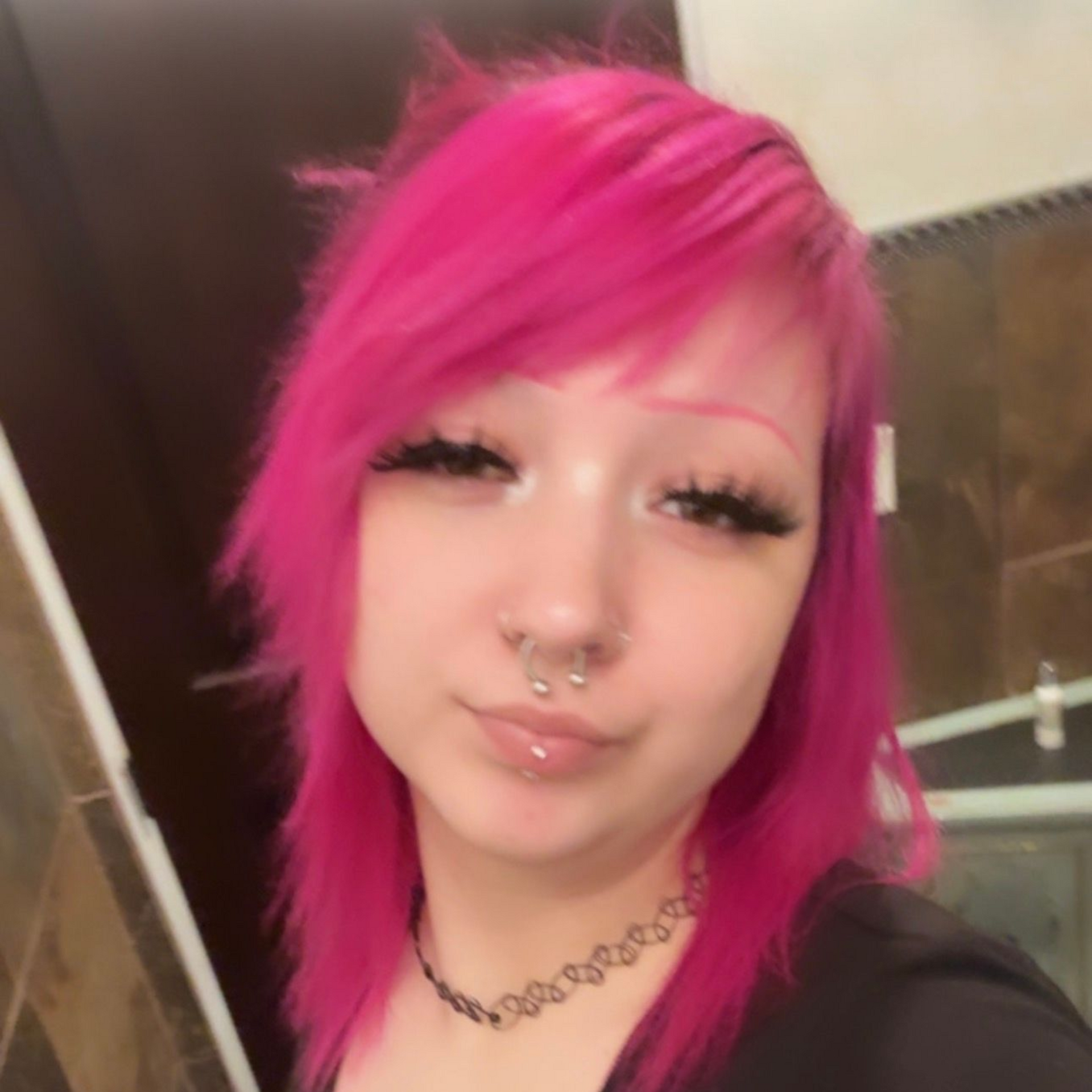 Woman with dark hair, nose ring, wearing a necklace, smiling in a car.