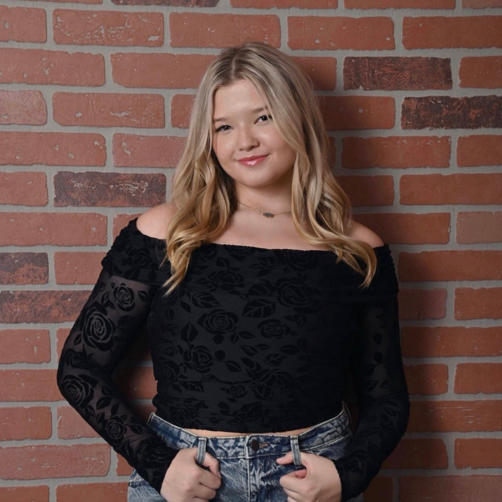 Blonde woman with wavy hair, wearing makeup, looking towards the camera.