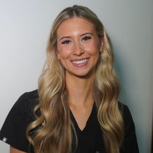 Blonde woman smiling, wearing lipstick, dark eye makeup, outdoors at night.