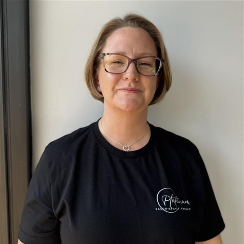Woman in glasses wearing a black t-shirt with a logo. She is smiling in front of a neutral-colored wall.