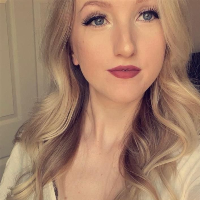 Blonde woman with wavy hair, wearing makeup, looking towards the camera.