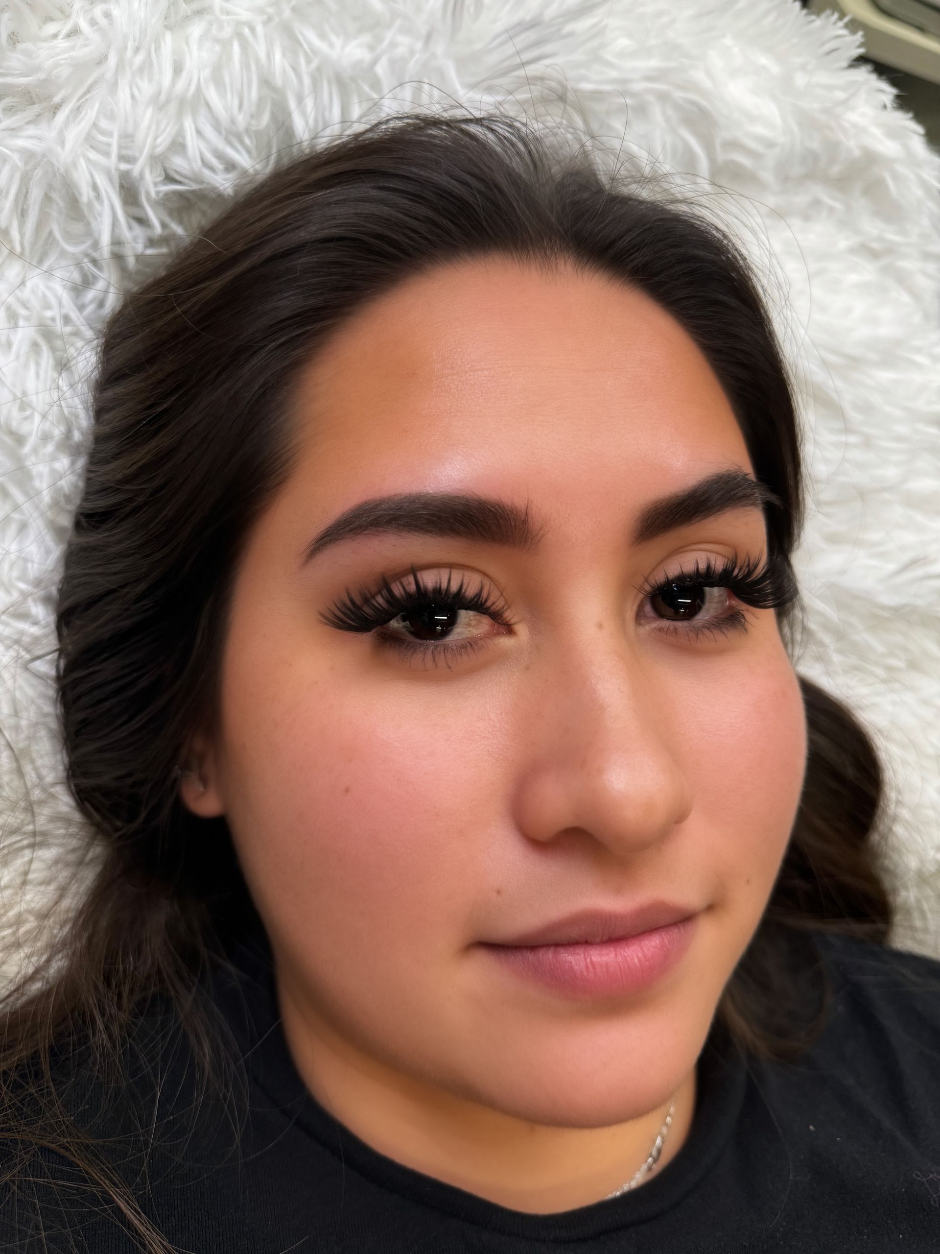 Platinum Salon and Spa brow shaping client with dark hair and long lashes, resting on a white fluffy pillow.