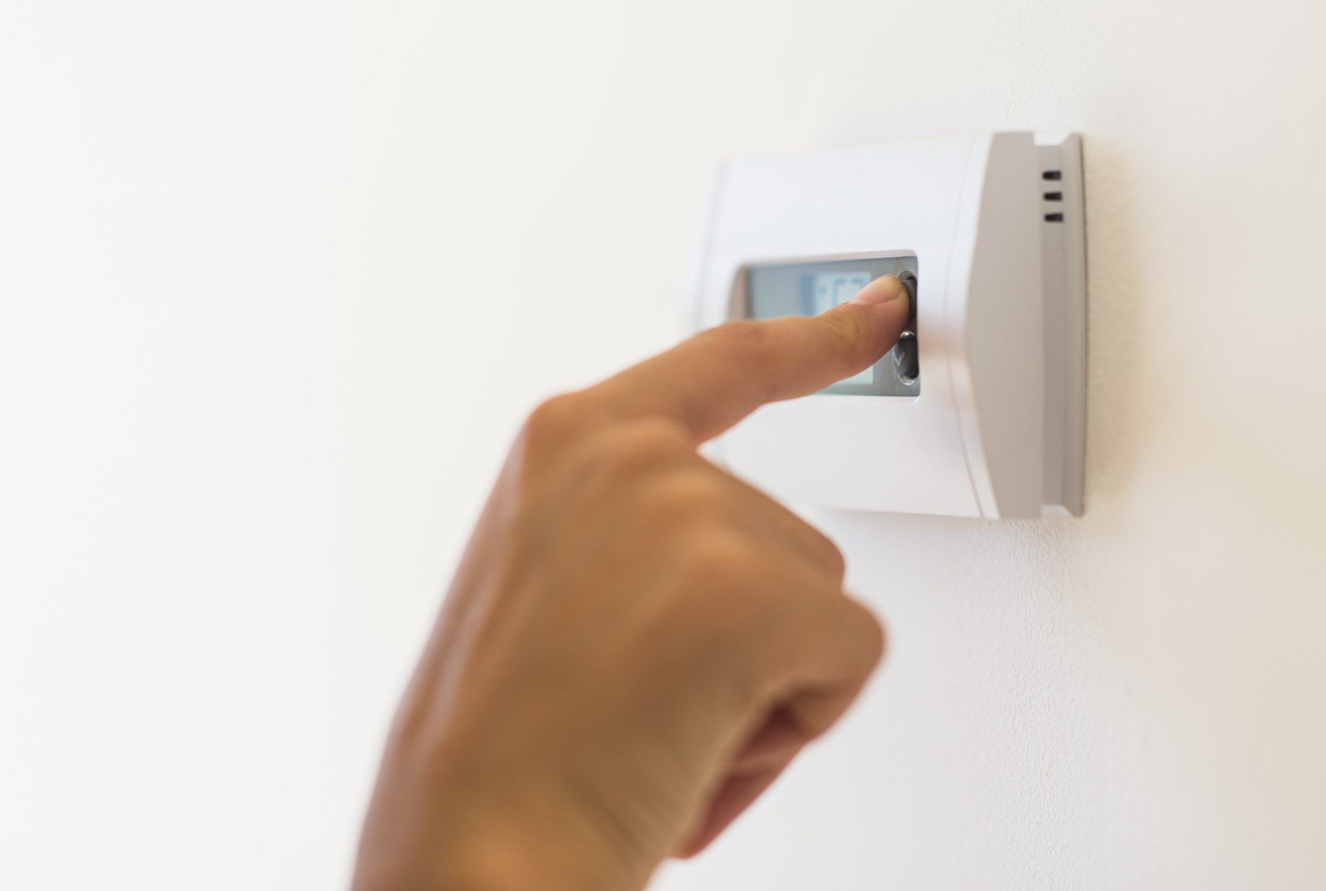 Hand adjusting a white thermostat on a white wall, likely changing the temperature setting.