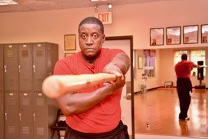 A man in a red shirt is holding a wooden stick in a gym.