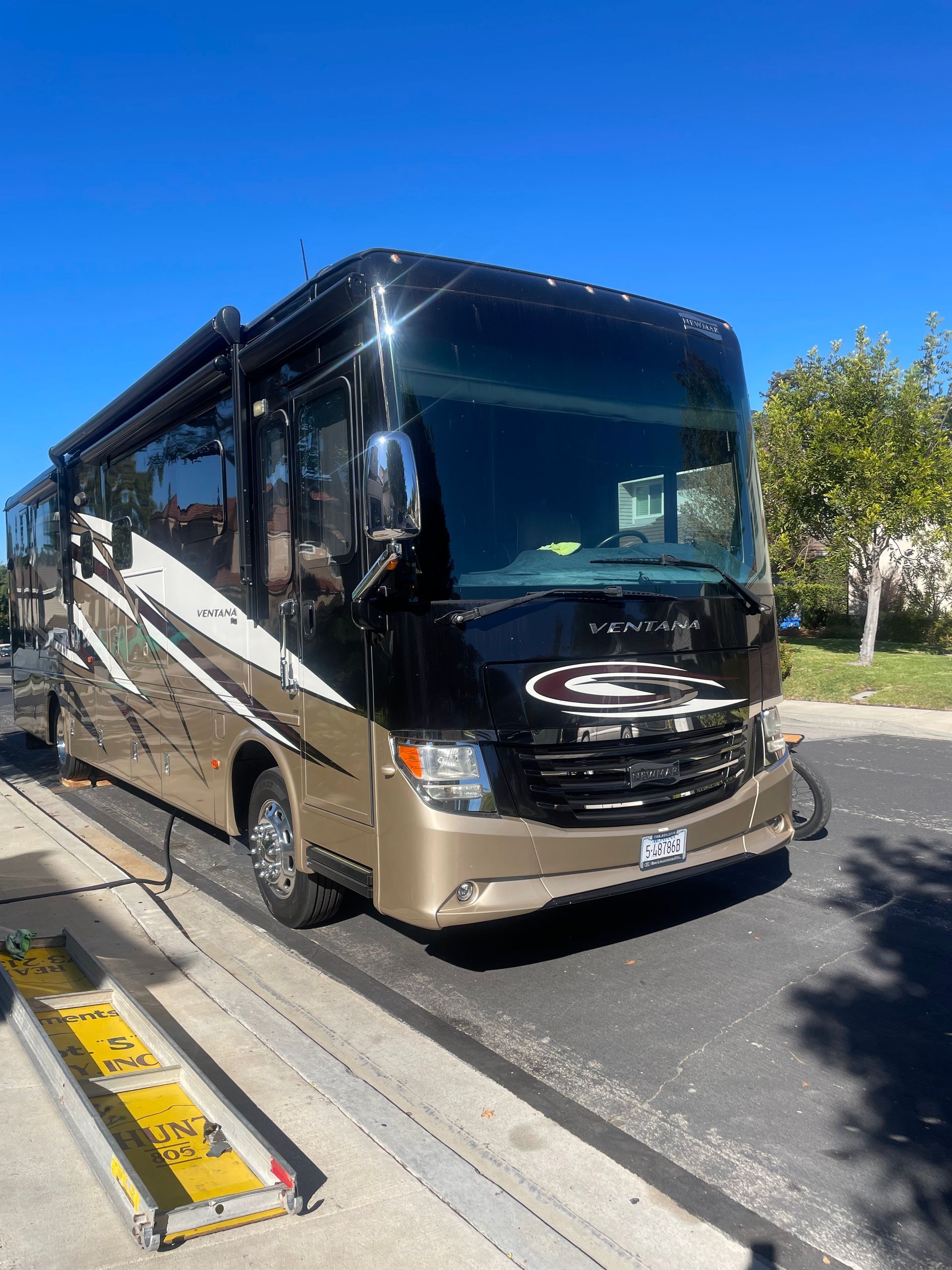 Black-and-tan luxury coach bus parked curbside on a sunny street under a blue sky