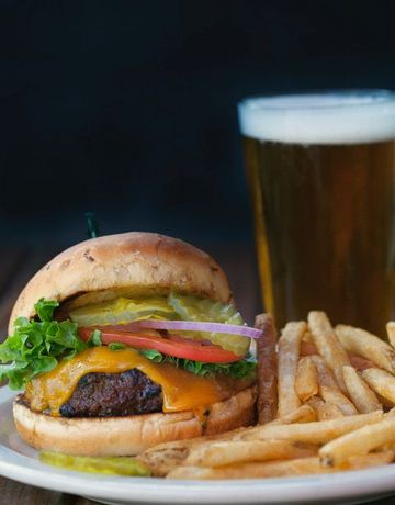 A hamburger and french fries on a plate next to a glass of beer.