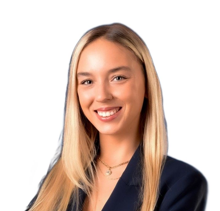 Mujer rubia sonriendo, vistiendo un blazer azul marino, collar dorado y sobre un fondo blanco.