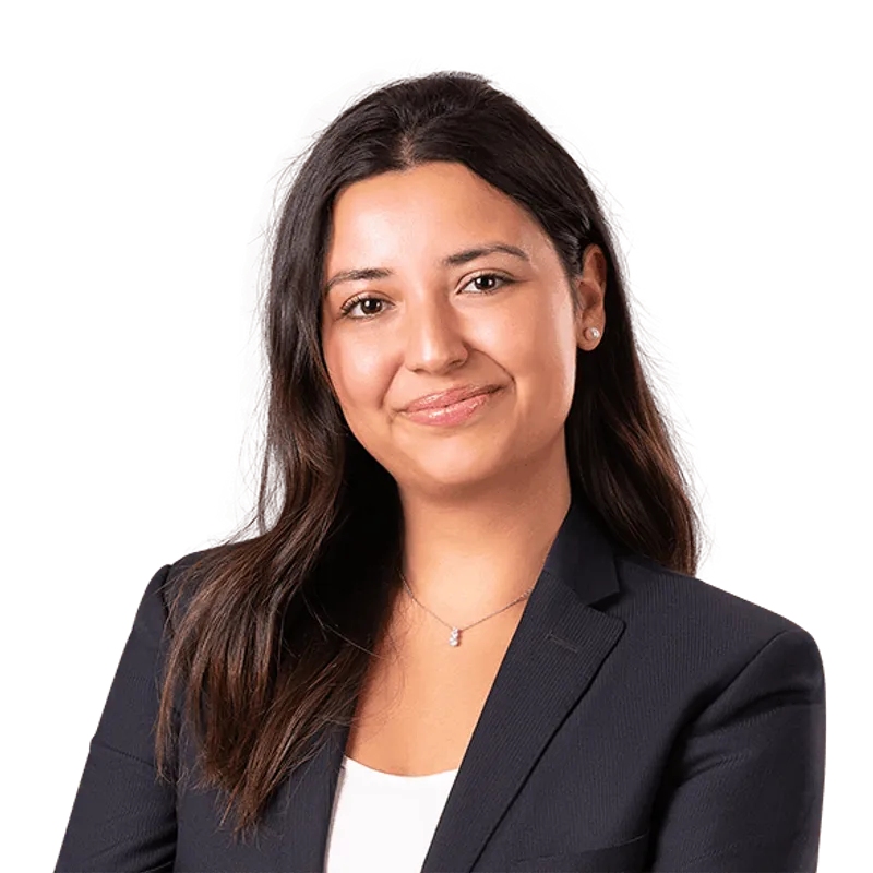 Una mujer de cabello oscuro con un blazer azul marino sonríe, vistiendo una blusa blanca, contra un fondo blanco.