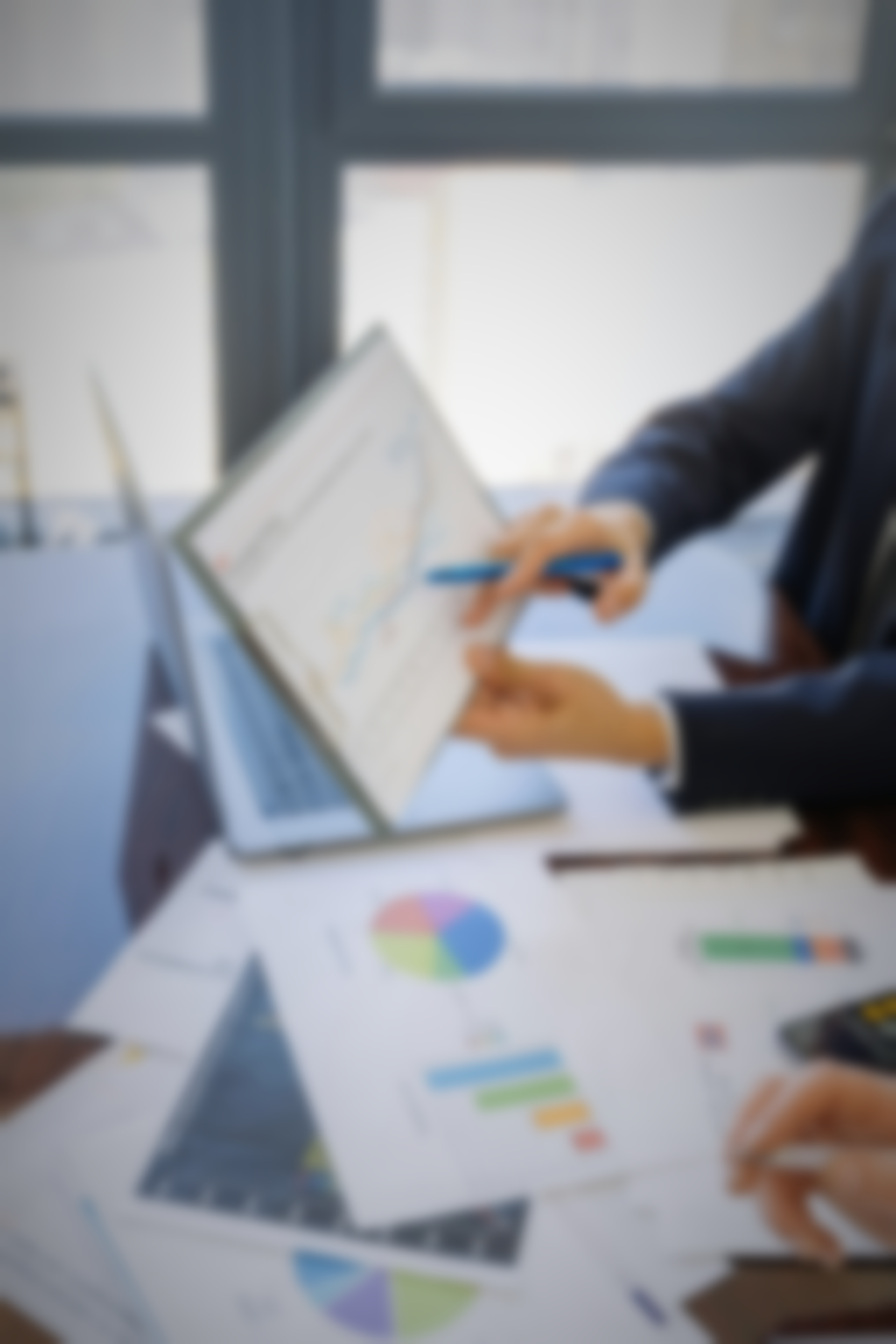 Una persona de traje señala un gráfico en la pantalla de una computadora portátil durante una reunión de negocios. Hay otros gráficos y una computadora portátil sobre la mesa.