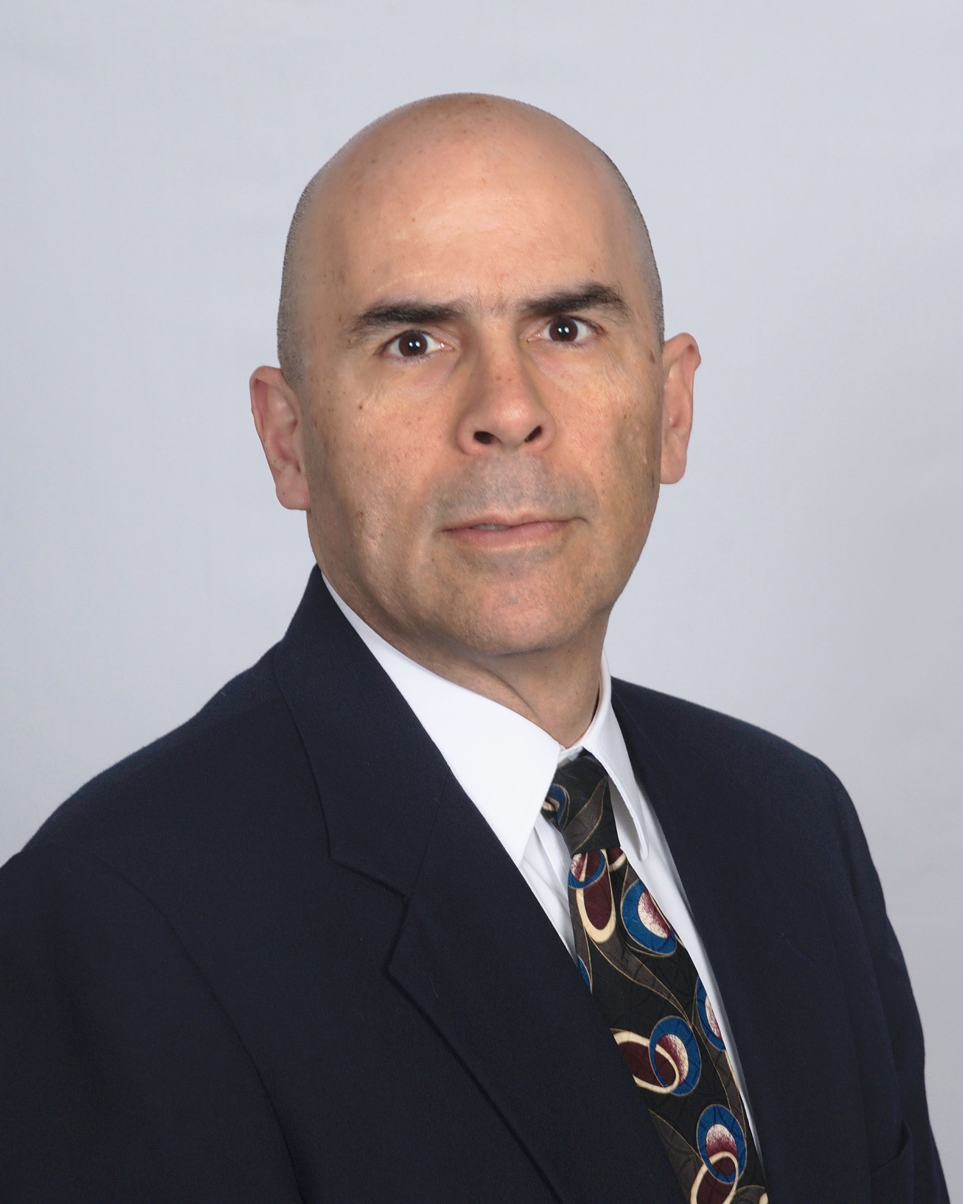 A bald man in a suit and tie looks at the camera