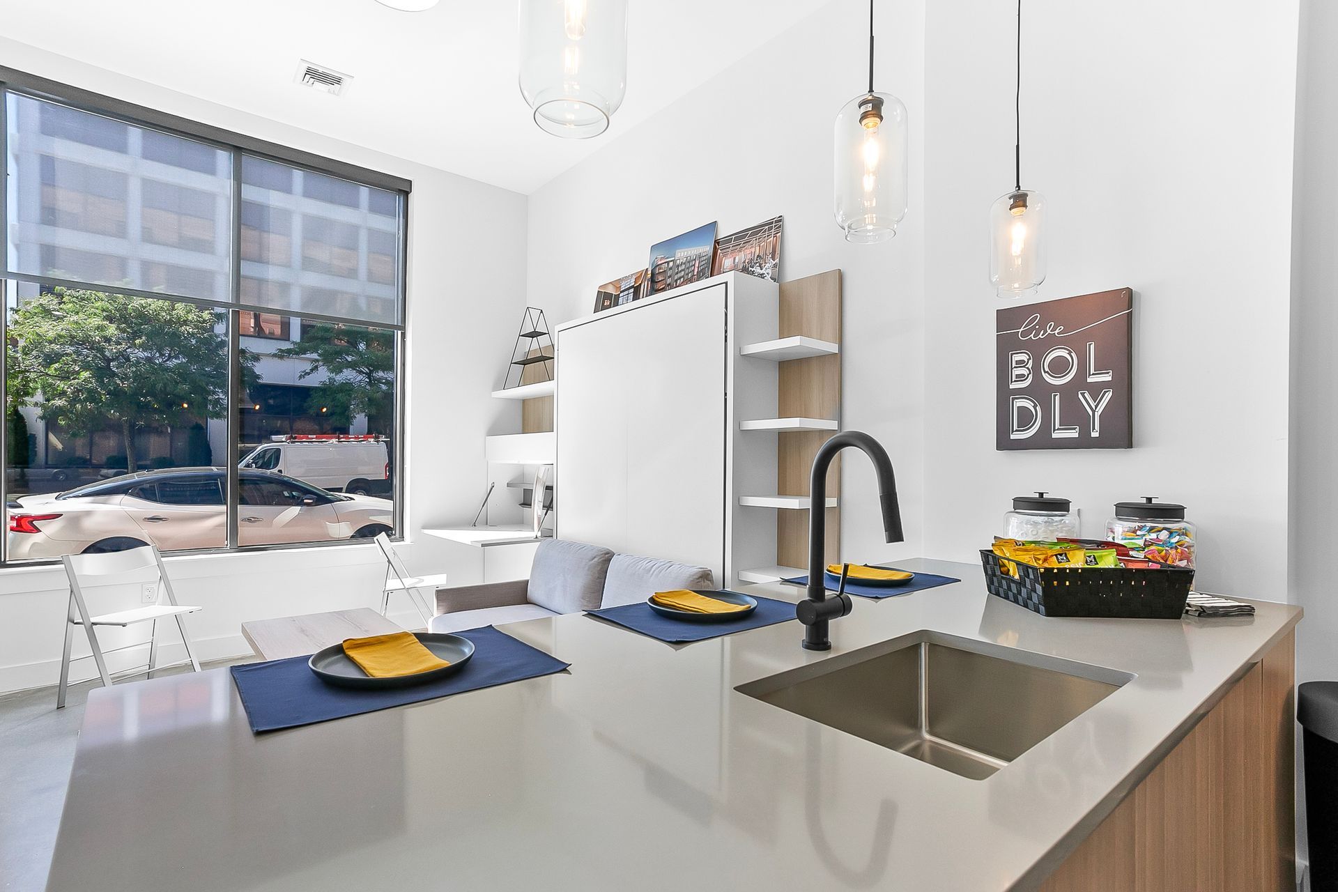 Modern studio apartment with kitchen island, large window, and built-in shelving.