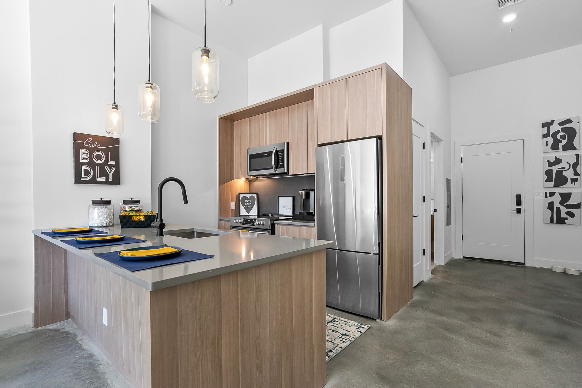 Modern kitchen with island, stainless steel refrigerator, and light wood cabinets.