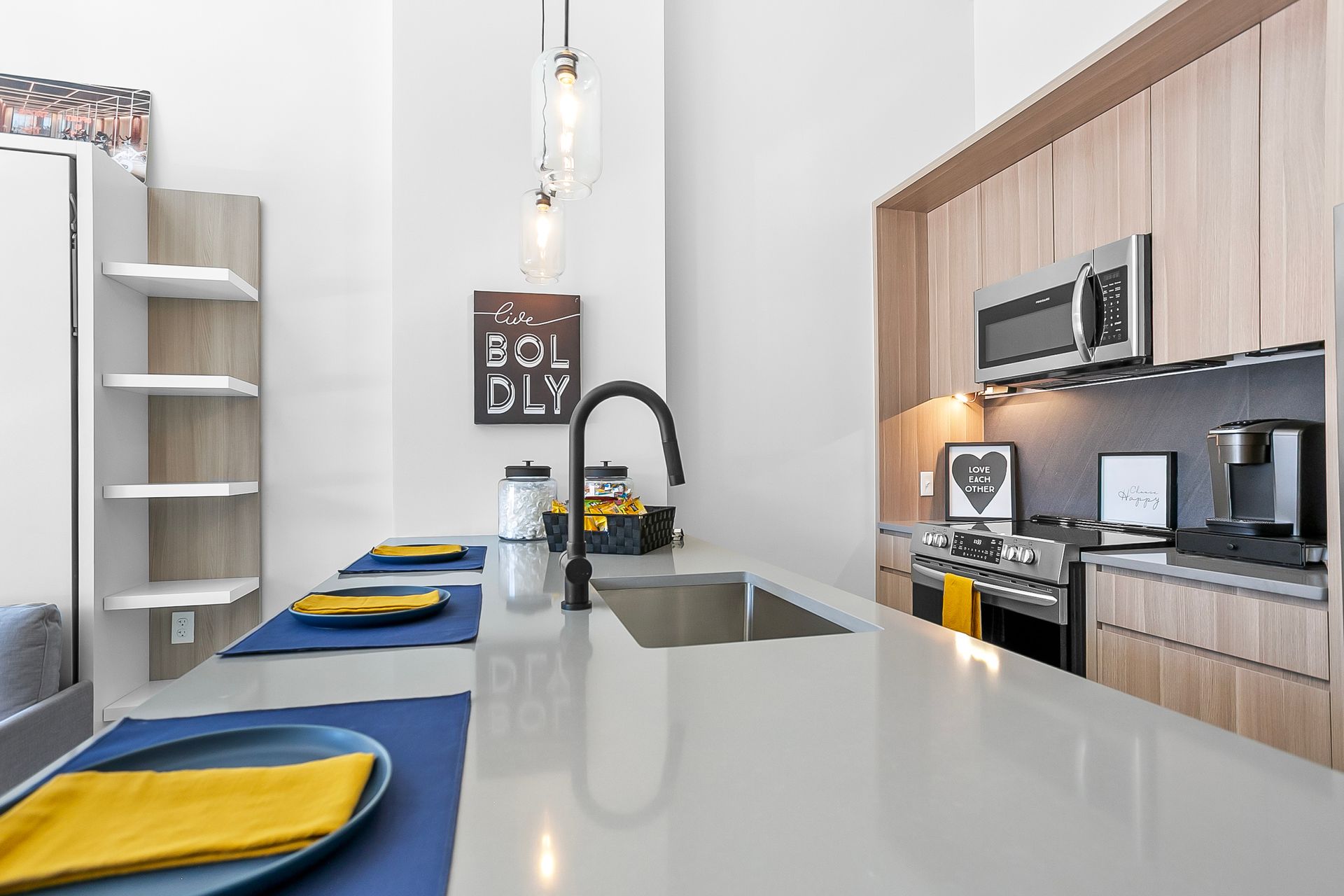 Modern kitchen with island, sink, oven, and wood cabinets. Yellow and blue place settings.