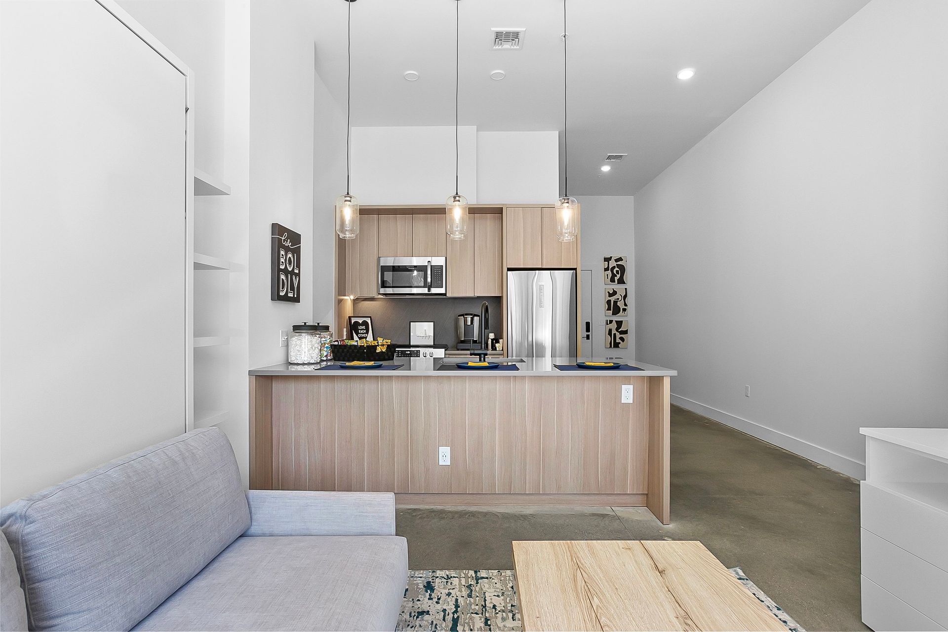 Small modern apartment with kitchen, sofa, and light wood cabinetry.