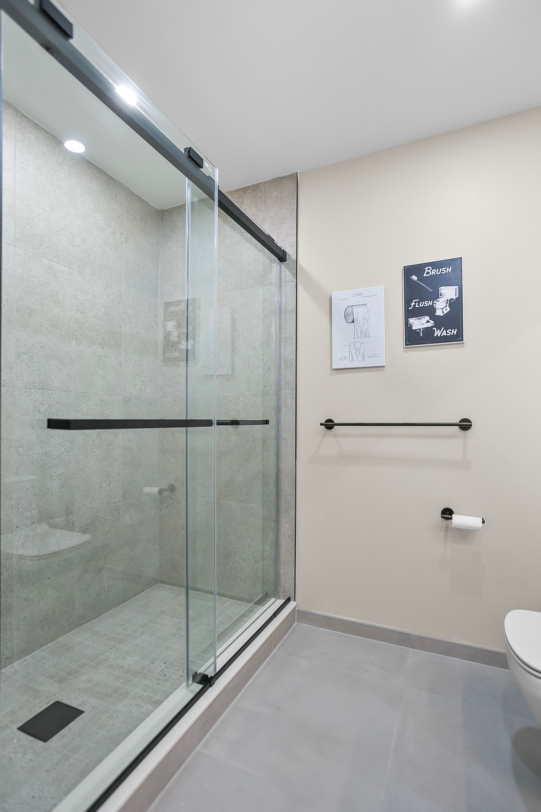 Modern bathroom with glass shower door, light gray walls, and tile flooring.