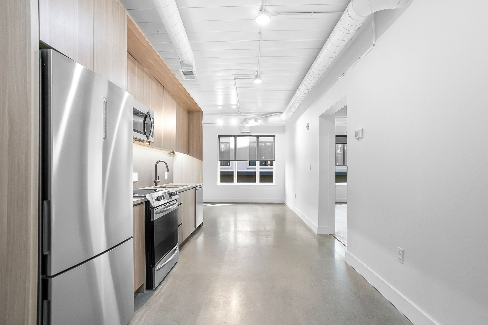 Modern kitchen with stainless steel appliances, light wood cabinets, and concrete floor.