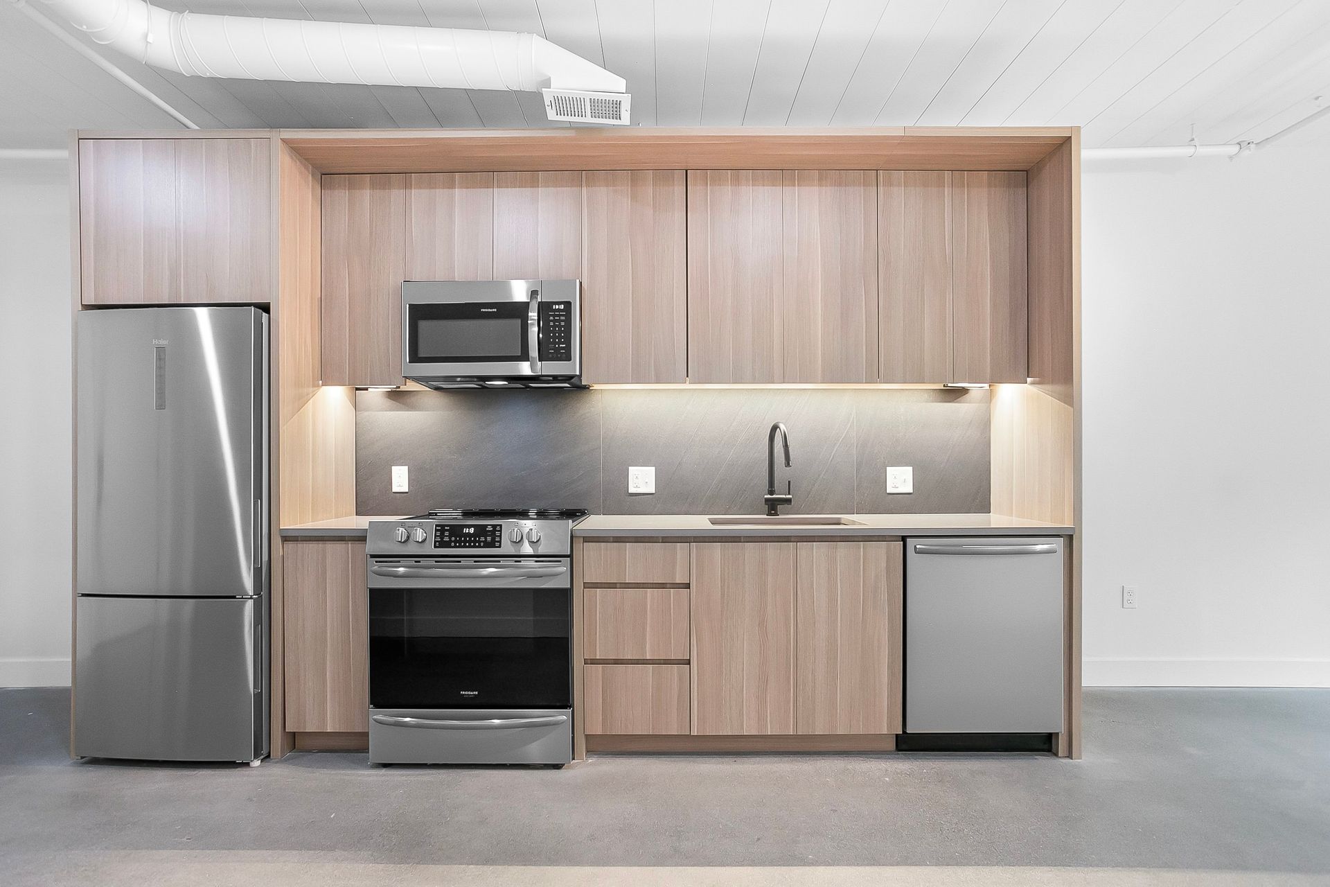 Modern kitchen with light wood cabinets, stainless steel appliances, and a gray backsplash.