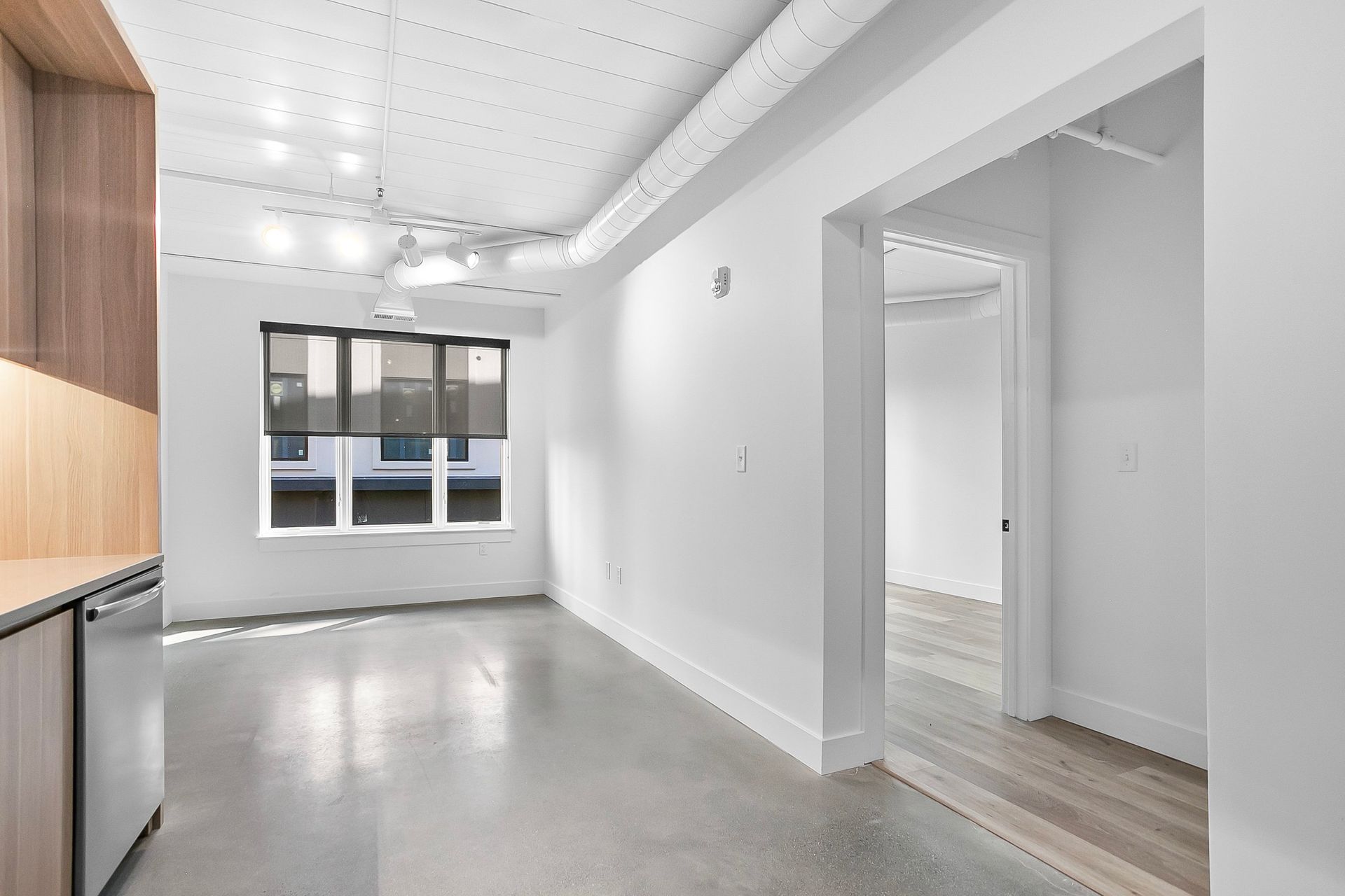 Empty, modern apartment interior with concrete floor, white walls, and a window.