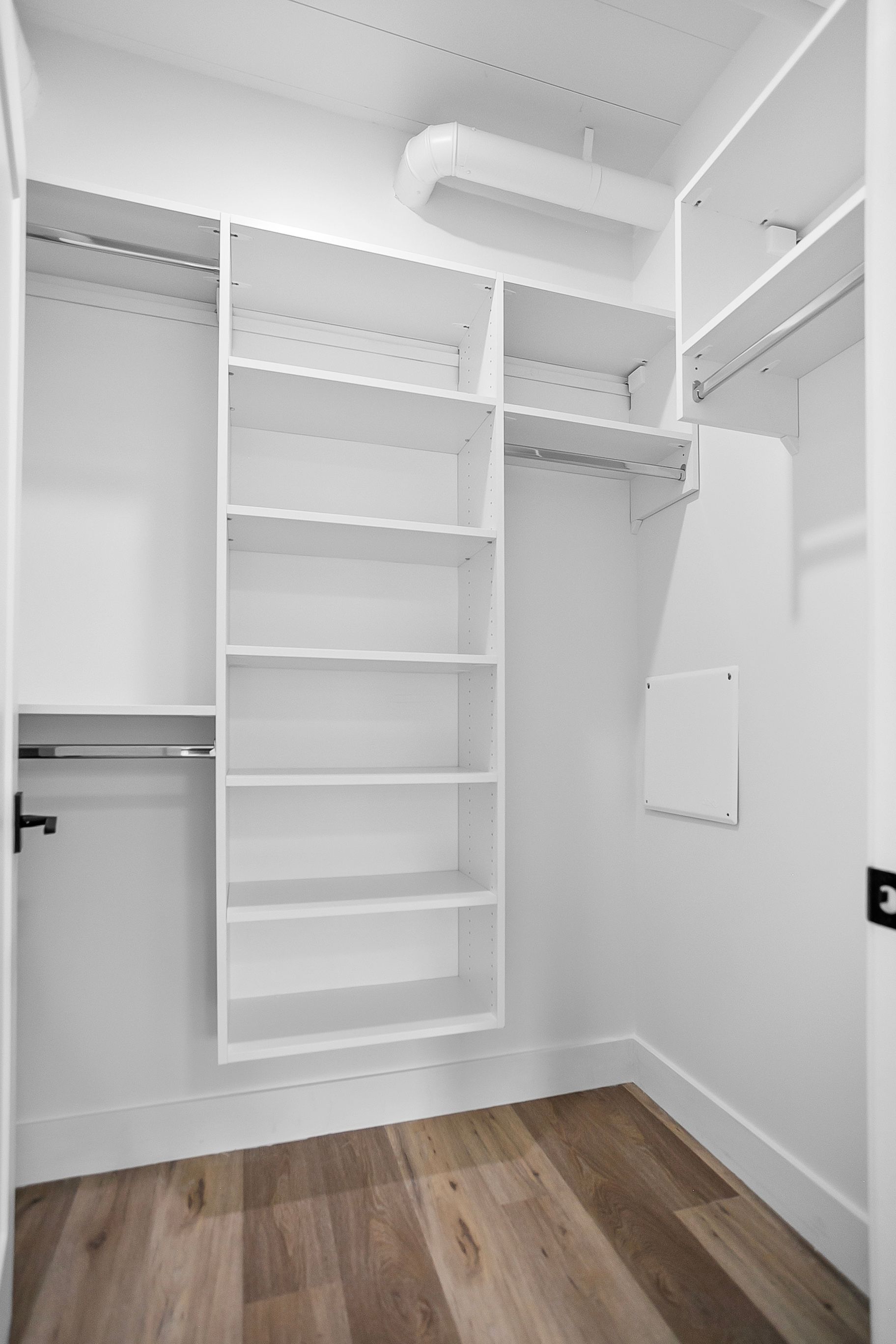 White walk-in closet with shelves, hanging rods, and hardwood floors.