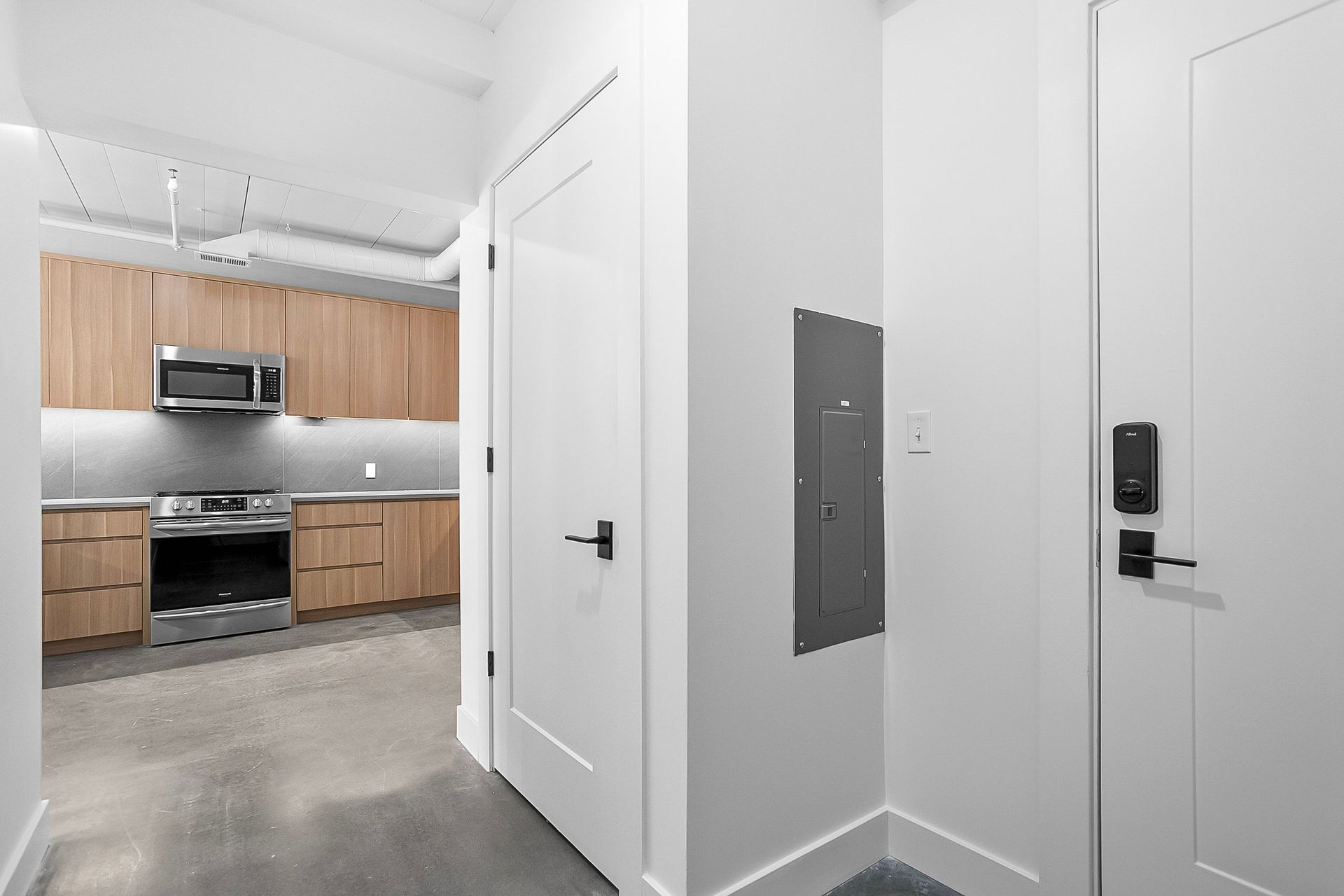 Hallway with white doors, gray floor, kitchen visible in the distance with wood cabinets.