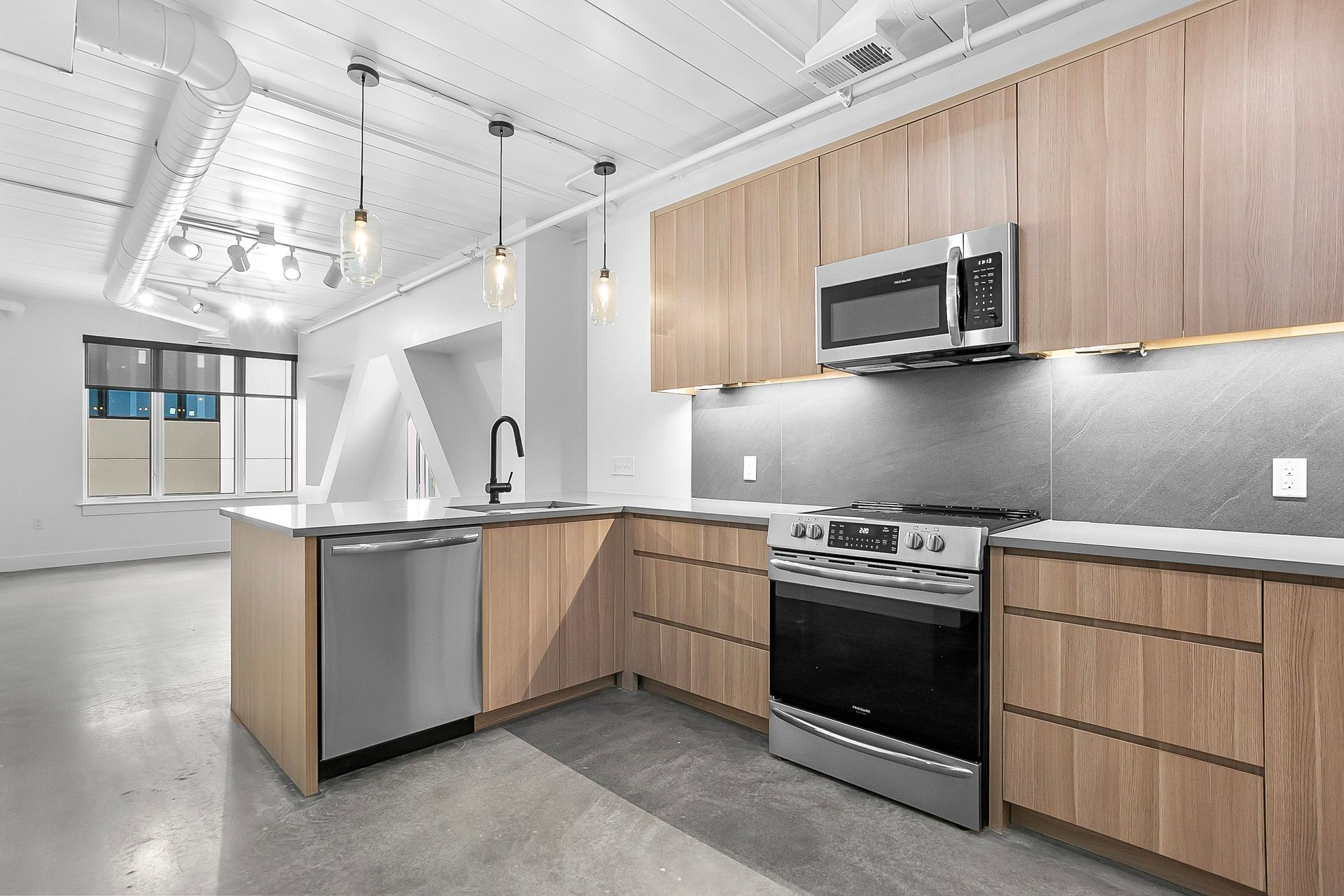 Modern kitchen with light wood cabinets, stainless steel appliances, and a gray countertop.