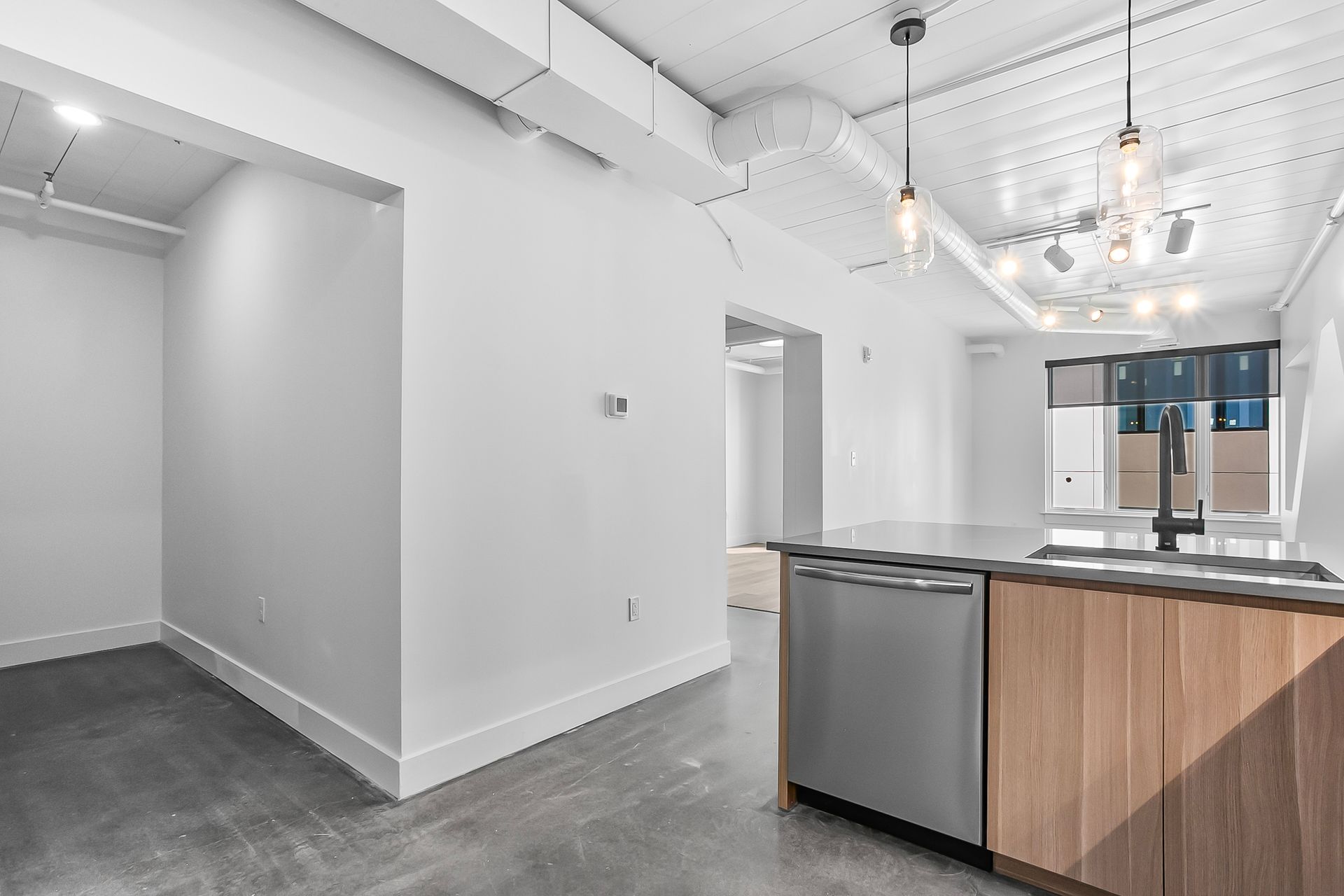 Modern kitchen with concrete floor, stainless steel appliances, and wood cabinets.