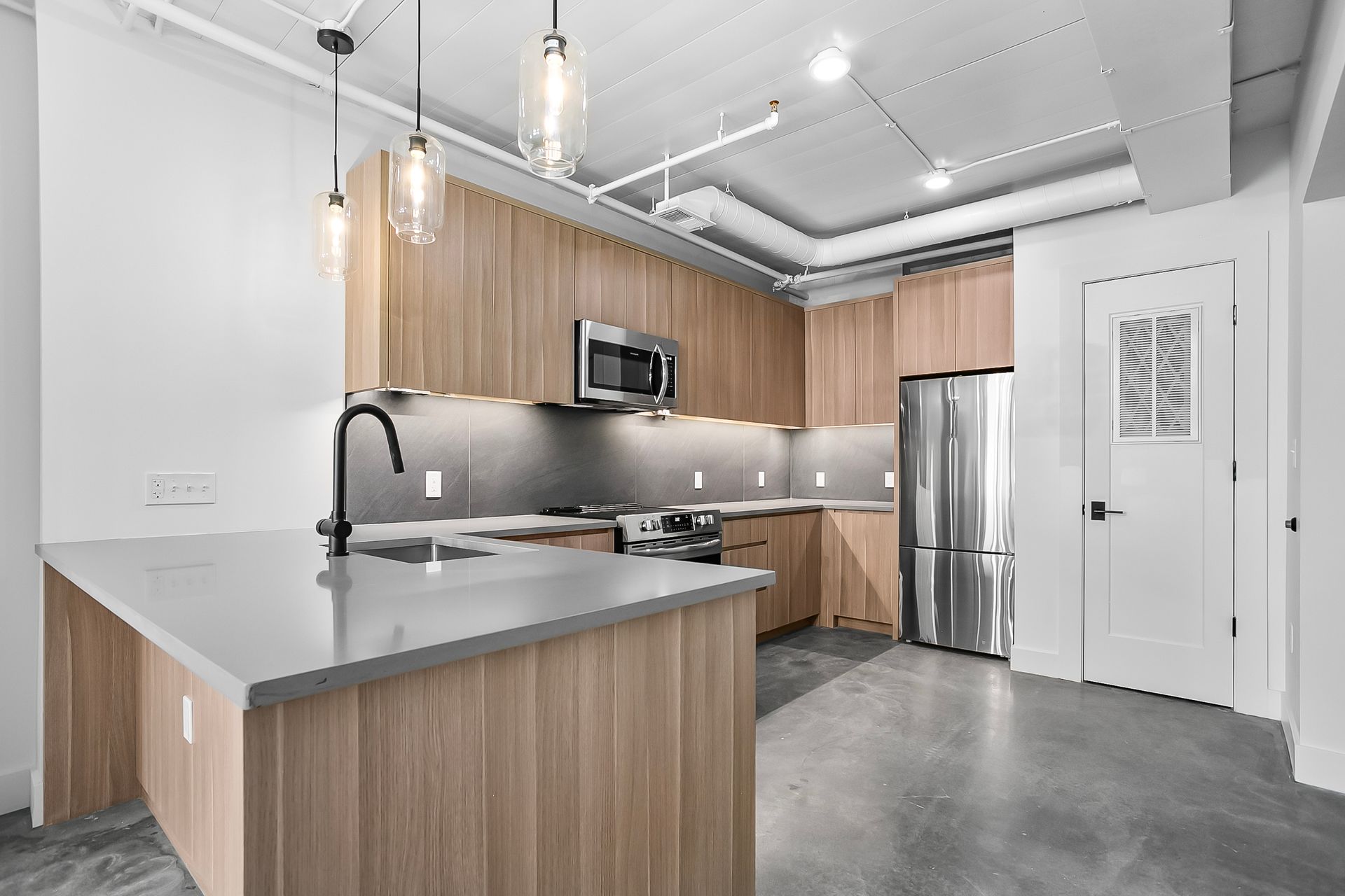 Modern kitchen with wood cabinets, stainless steel appliances, and gray countertops.