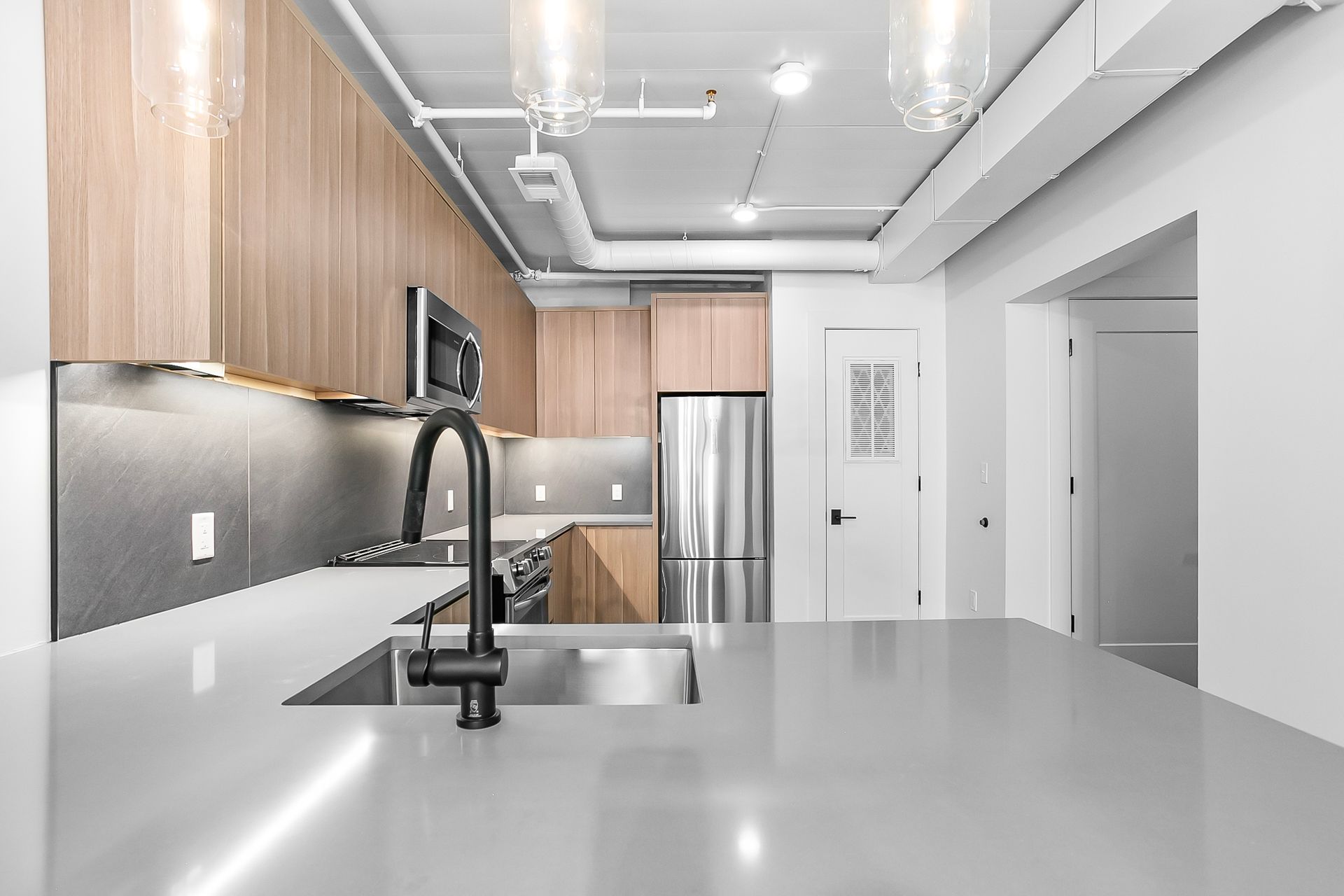 Modern kitchen with light wood cabinets, stainless steel appliances, and a gray countertop.