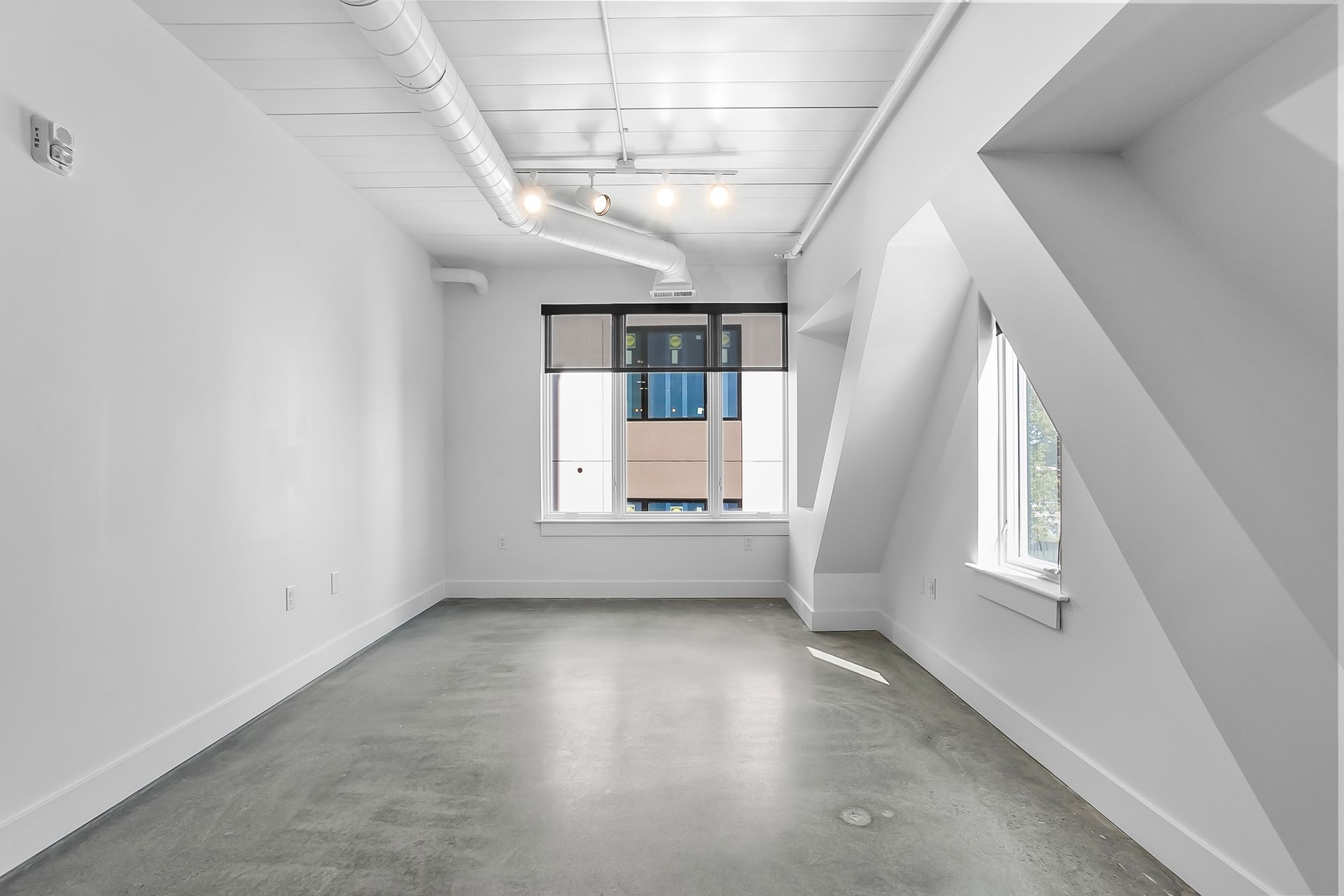 Empty white room with slanted ceiling, window, and concrete floor.