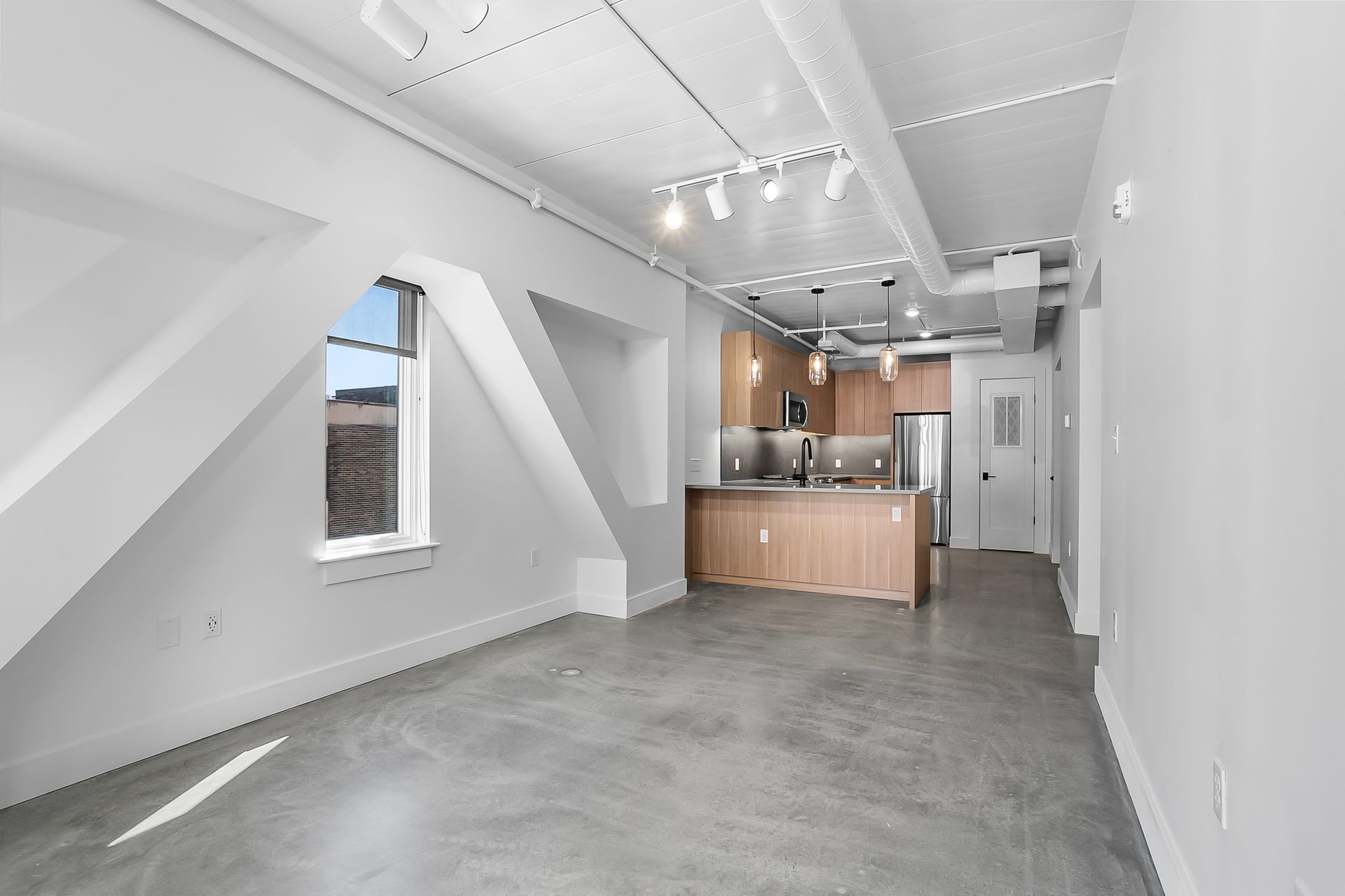 Empty apartment interior with angled walls, concrete floor, and small kitchen.