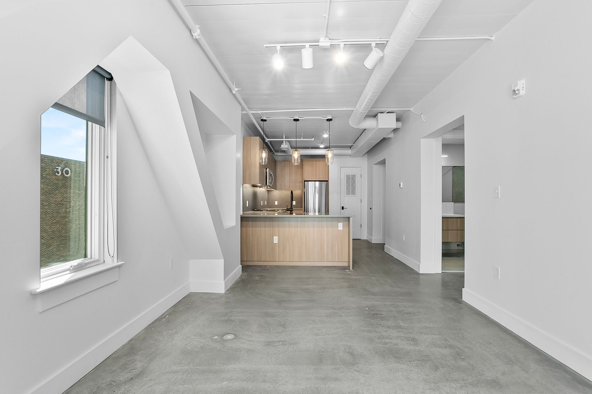 Modern apartment interior with concrete floor, kitchen, and large window.