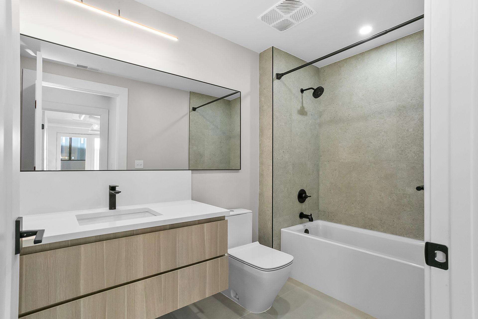 Modern bathroom with a light wood vanity, white toilet, tub and neutral-toned tile shower.