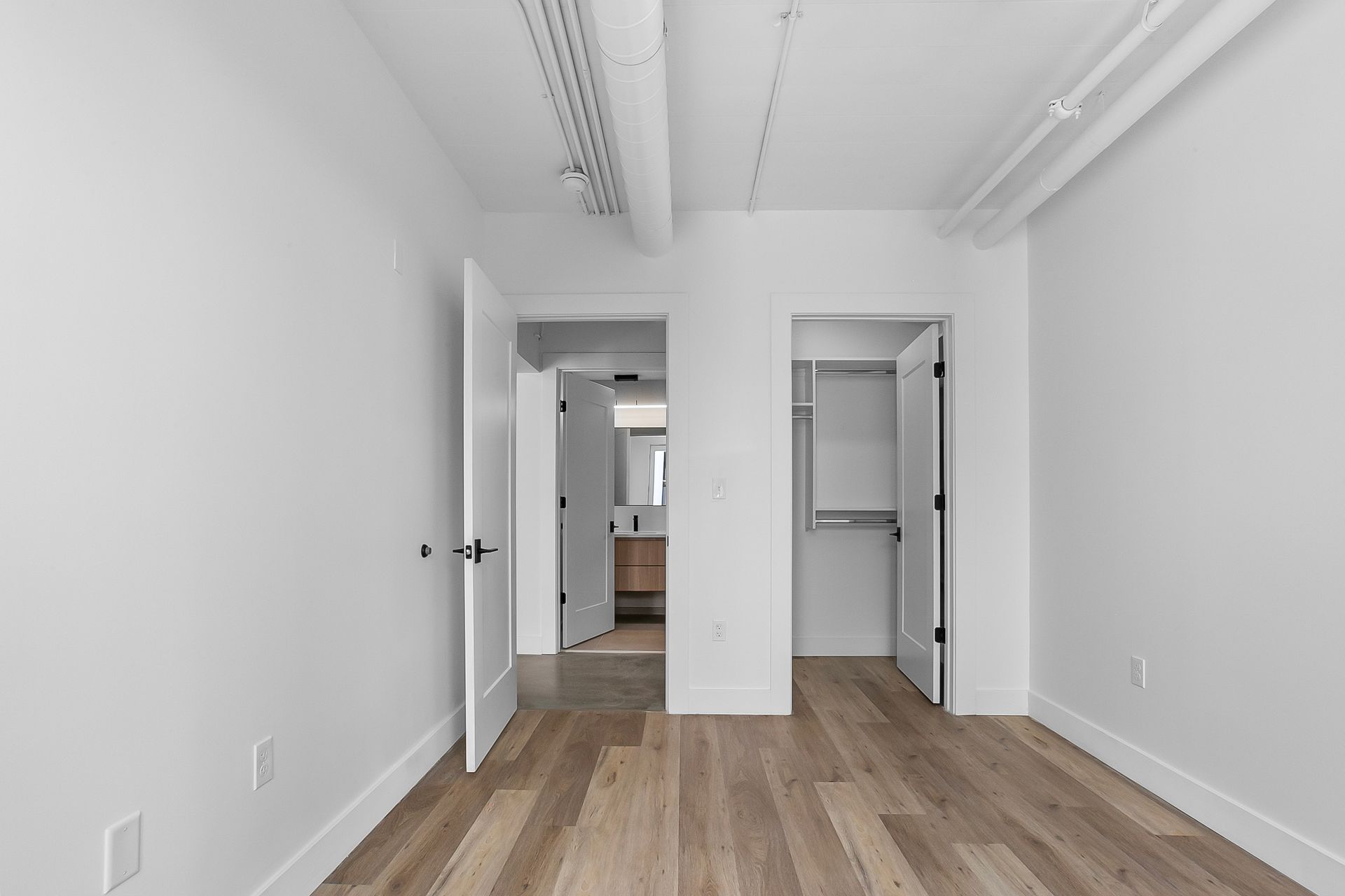 Empty room with wood floors, white walls, and open doors to a closet and bathroom.