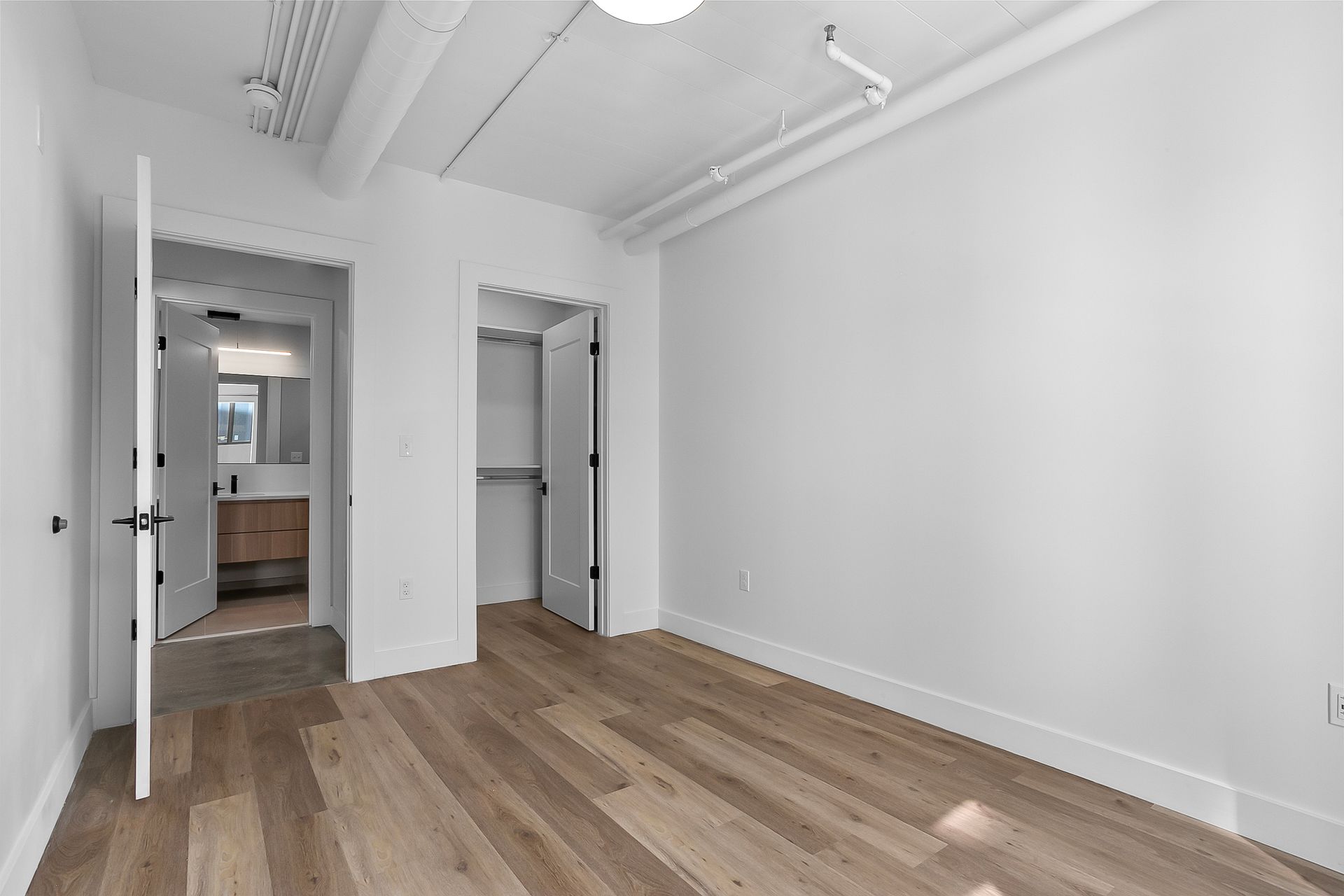 Empty room with wood floors, white walls, closet, and a doorway to a bathroom.