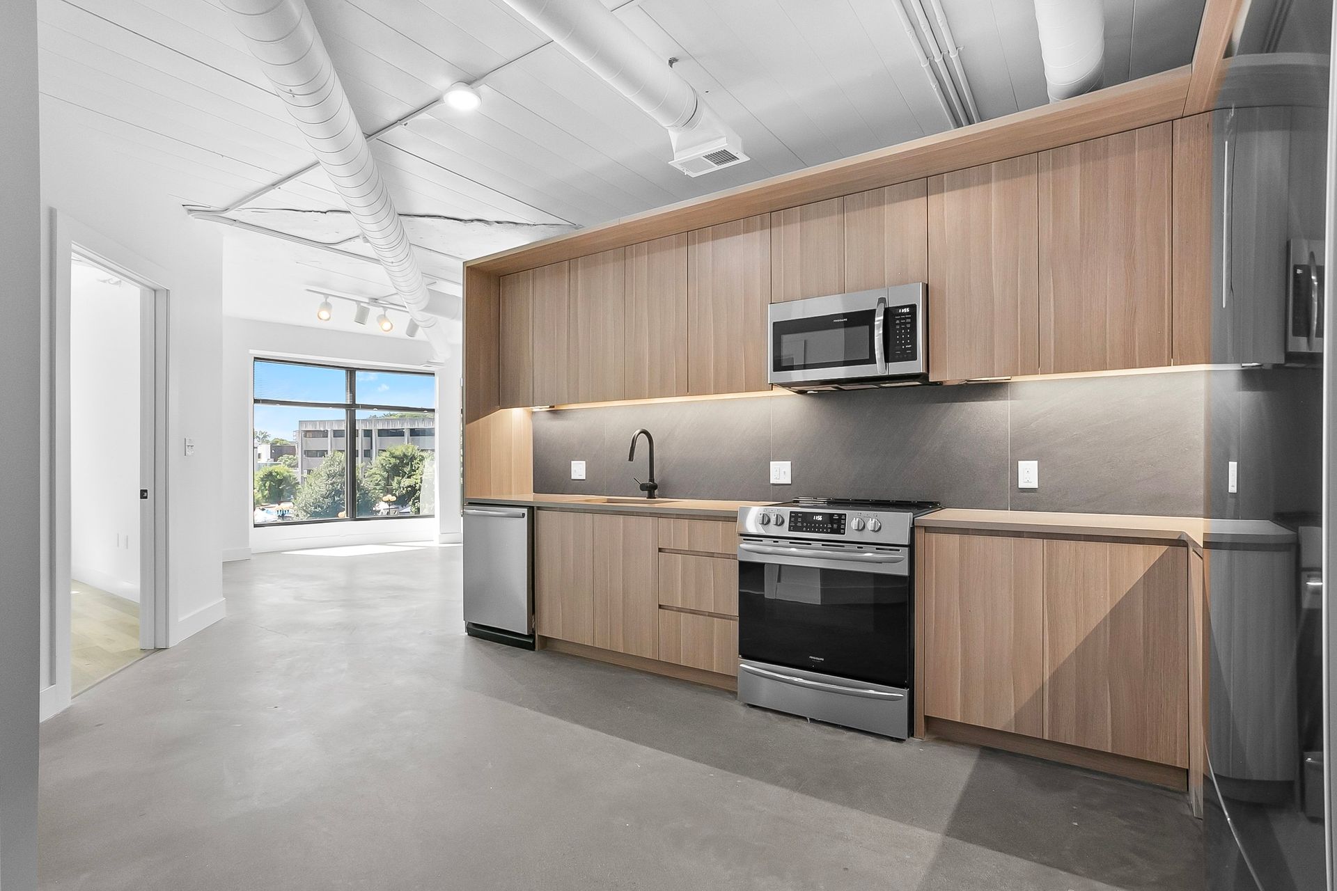 Modern kitchen with wood cabinets, stainless steel appliances, and concrete floor.