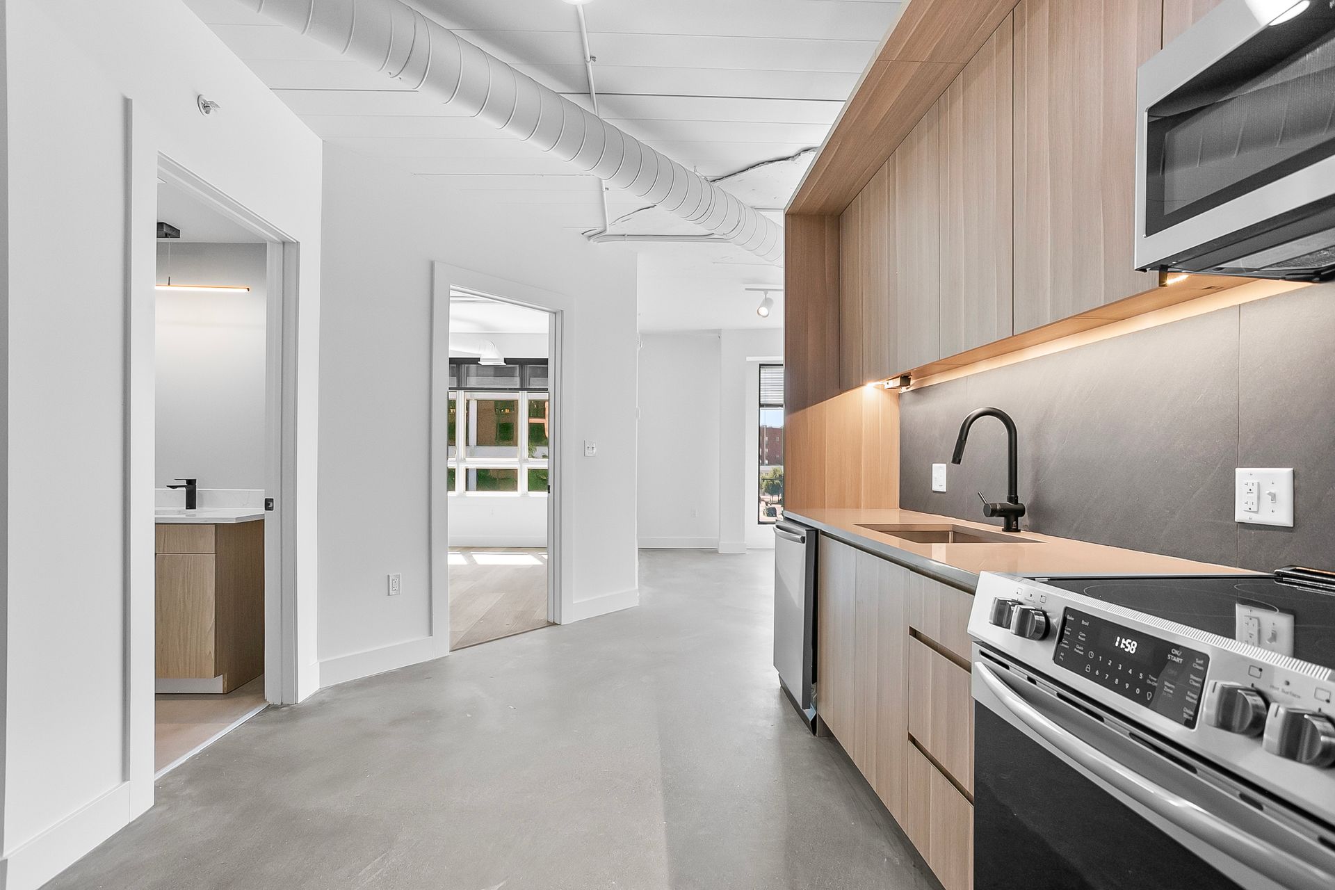 Modern kitchen with light wood cabinets, stainless steel appliances, and a hallway.