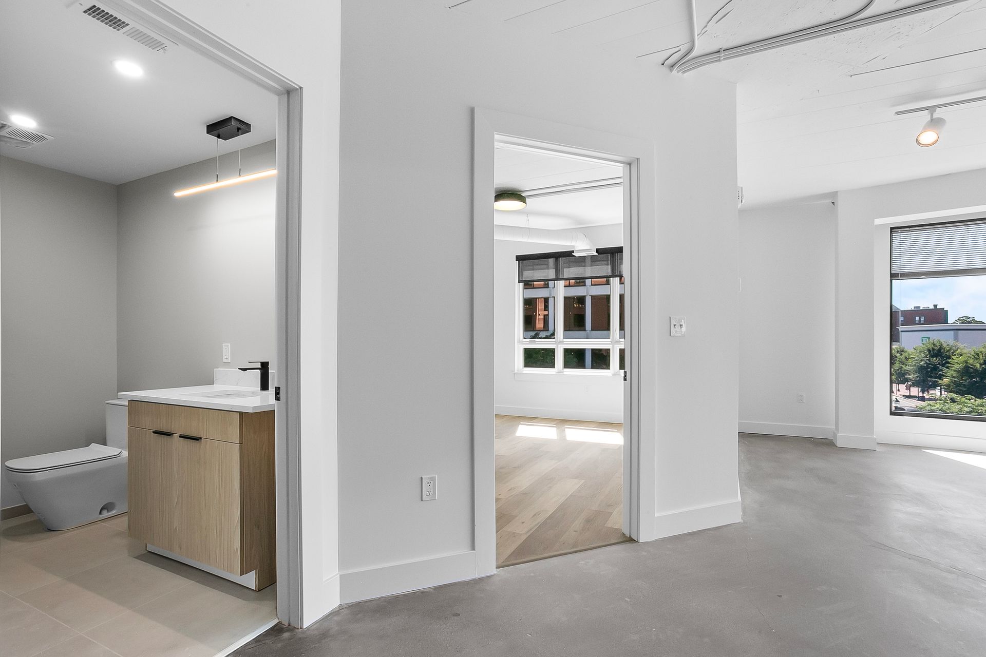 Open doorway leads to bright room with bathroom on the left and windows on the right.