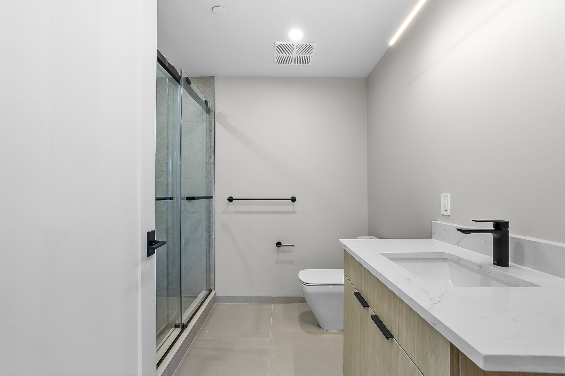 Modern bathroom with a glass shower, toilet, and vanity with a white countertop.